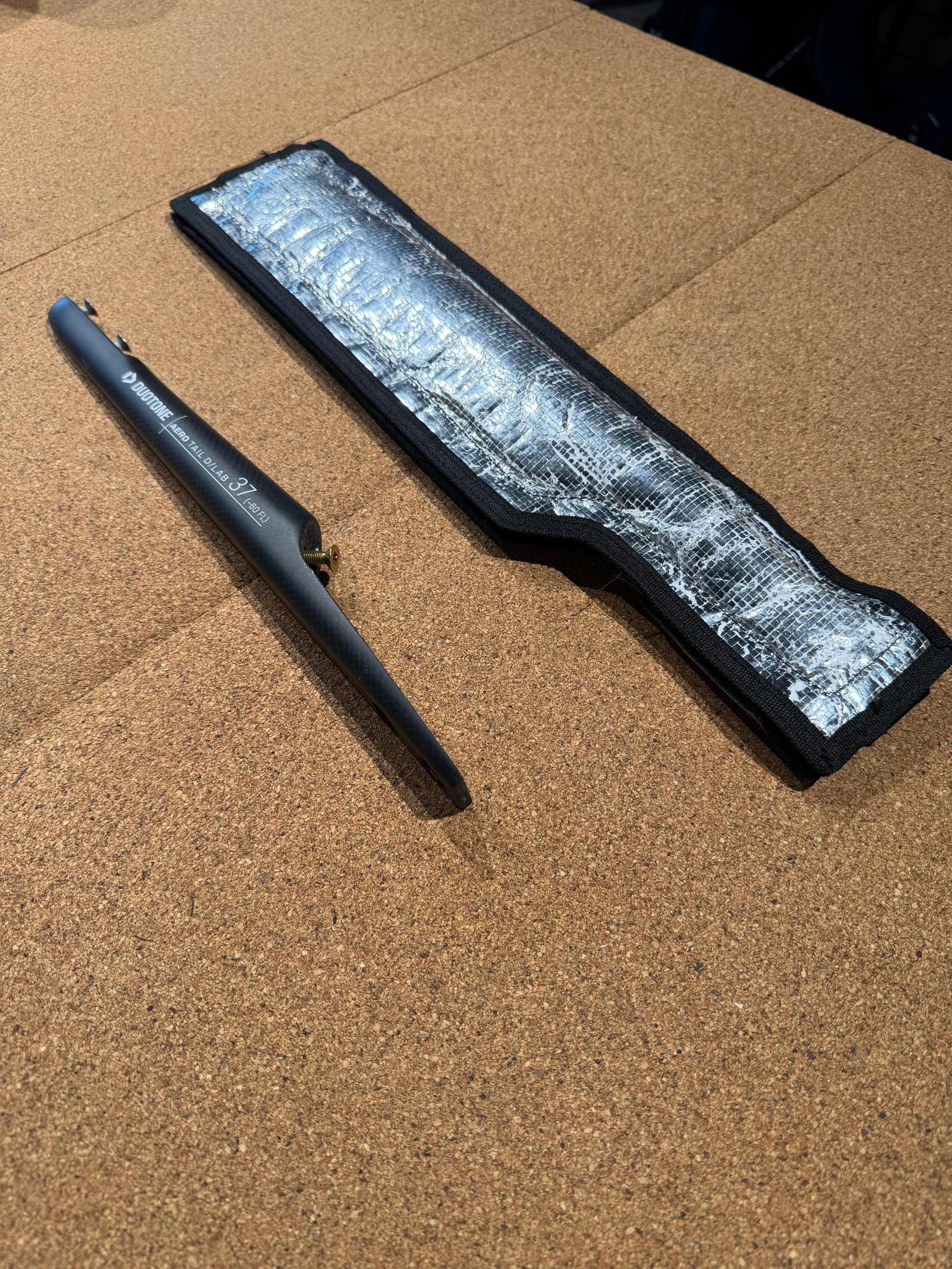 Black carbon Duotone Aero Tail D/LAB 37 fuselage with mounting bolt and protective silver sleeve on a cork surface.