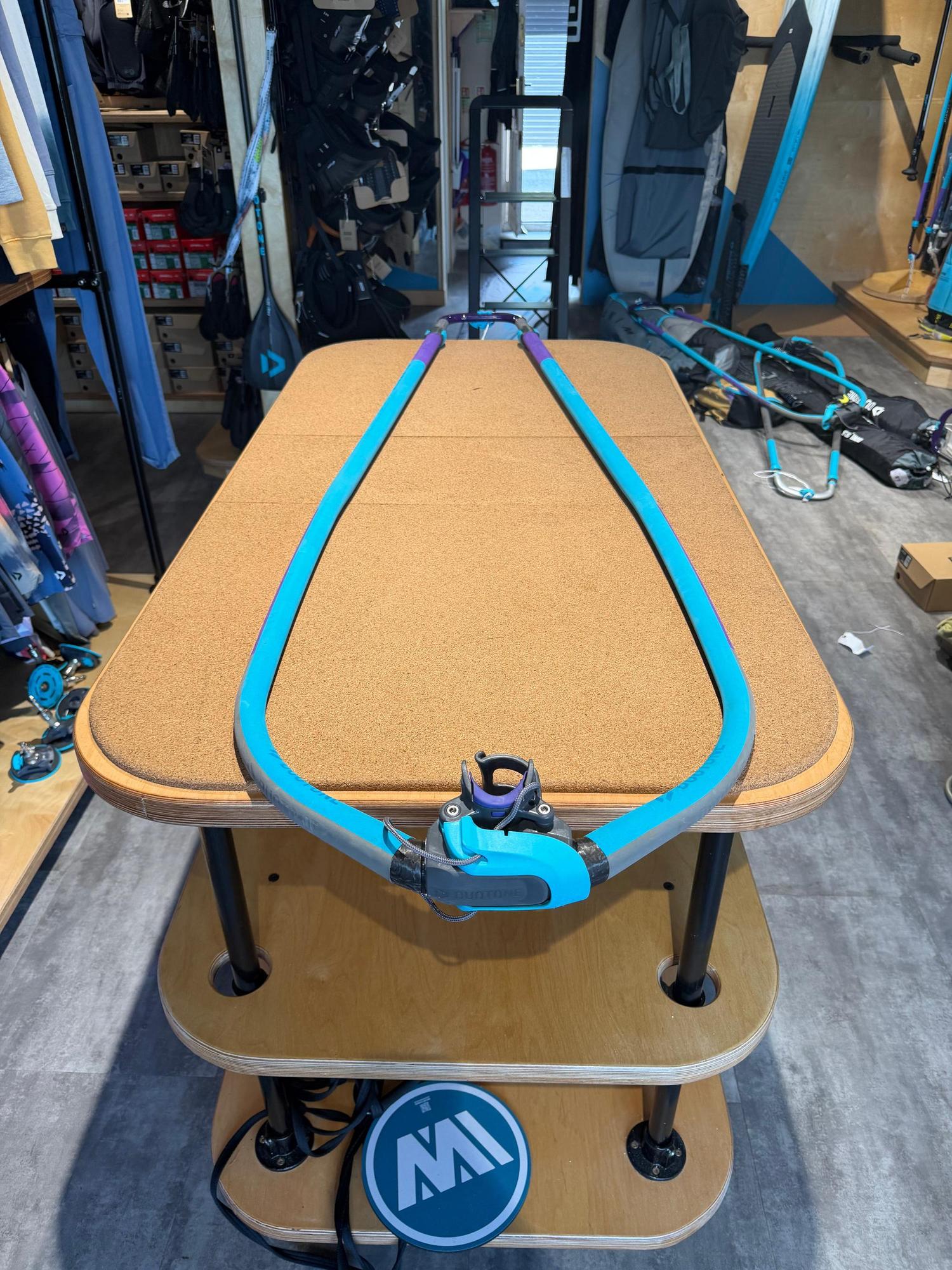 Used Duotone Platinum SLS 160-220 carbon windsurfing boom in turquoise and grey, displayed on a wooden workbench.