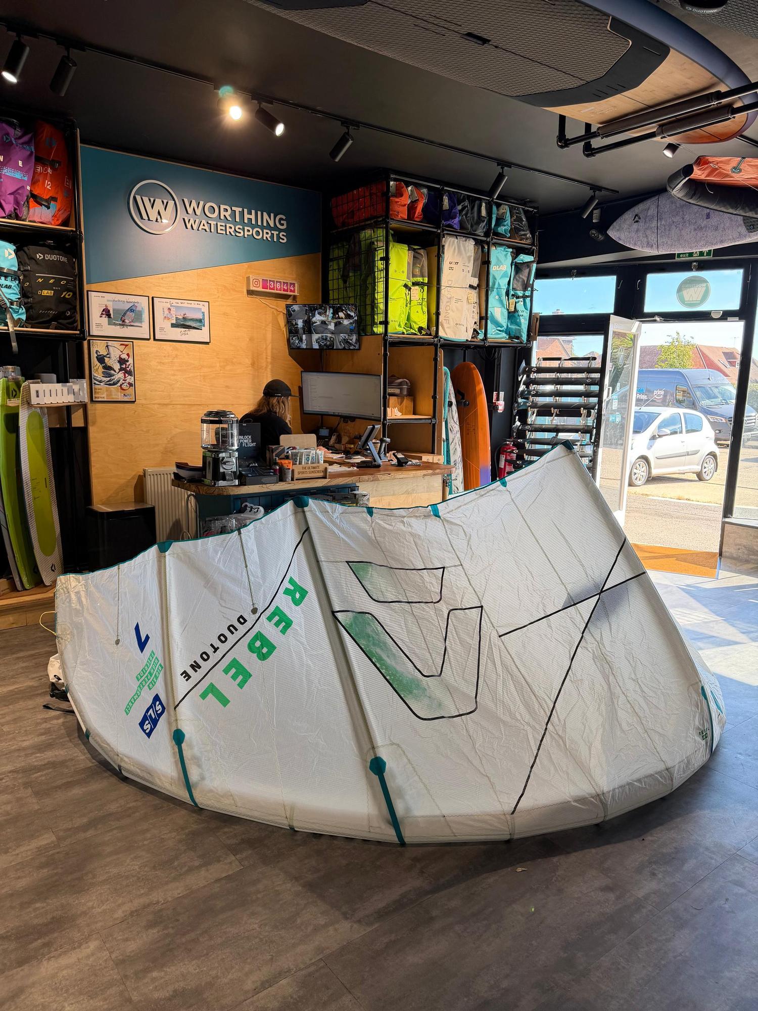 White 7m Duotone Rebel SLS Concept Blue kite with green branding, displayed on the floor of a watersports shop.