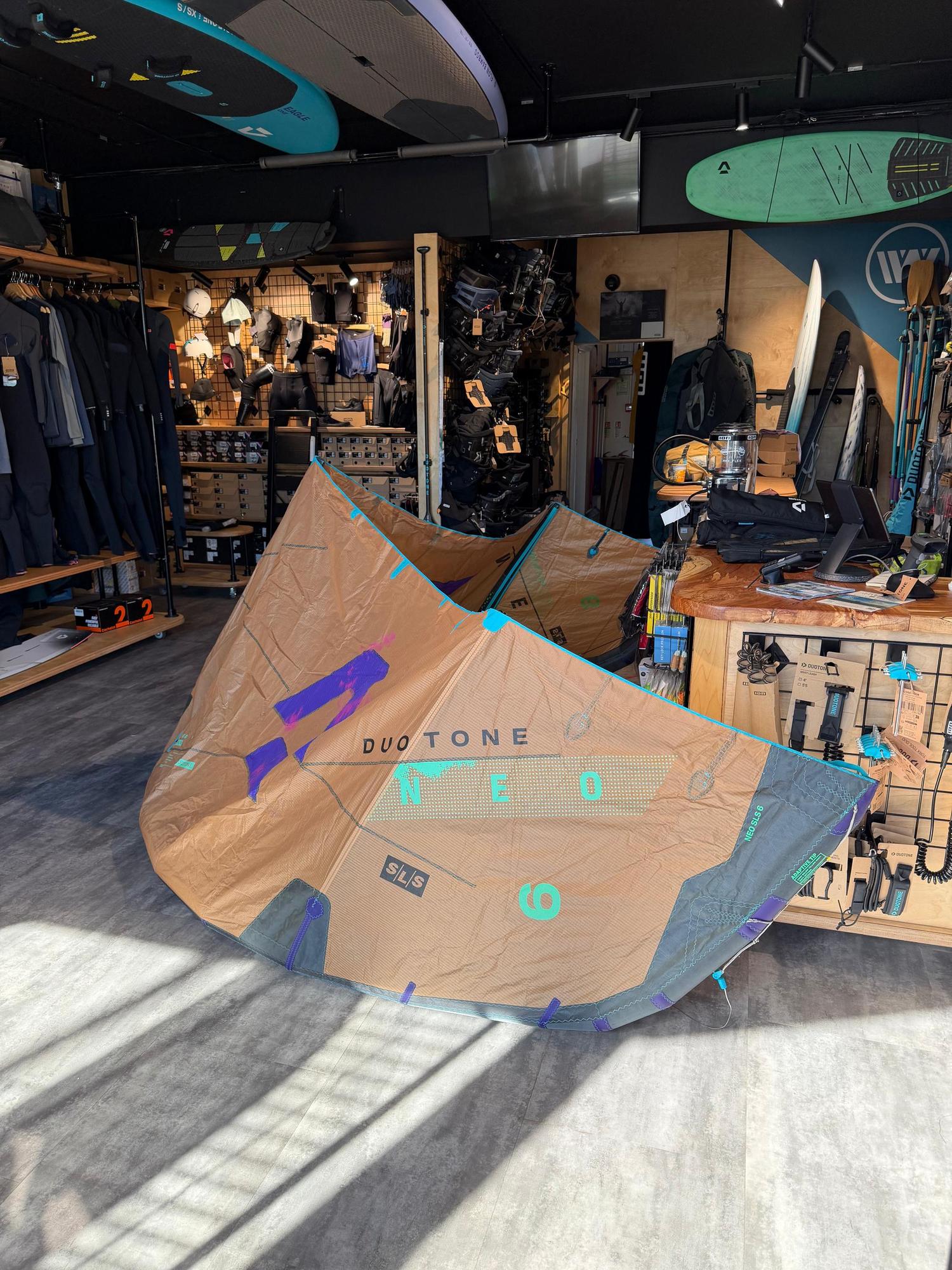 Used 6m Duotone Neo SLS wave kite in tan and teal, displayed in a shop with visible branding and performance materials.