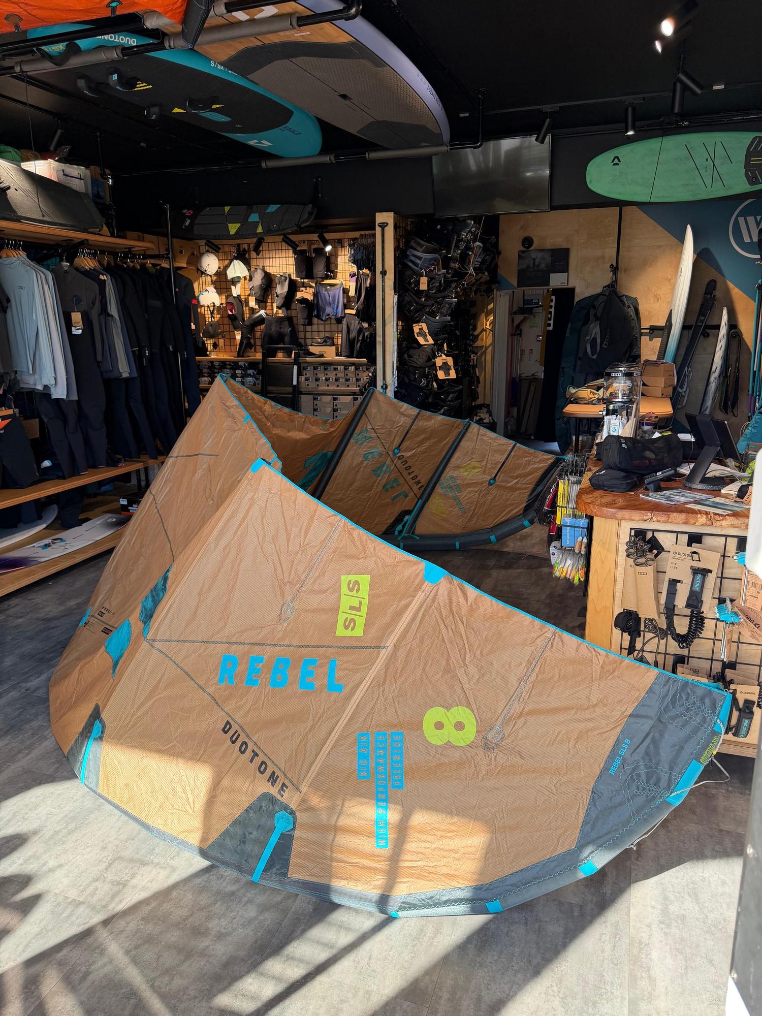Used 8m Duotone Rebel SLS big air kite in tan and teal, featuring high-performance Penta TX material in a retail store.