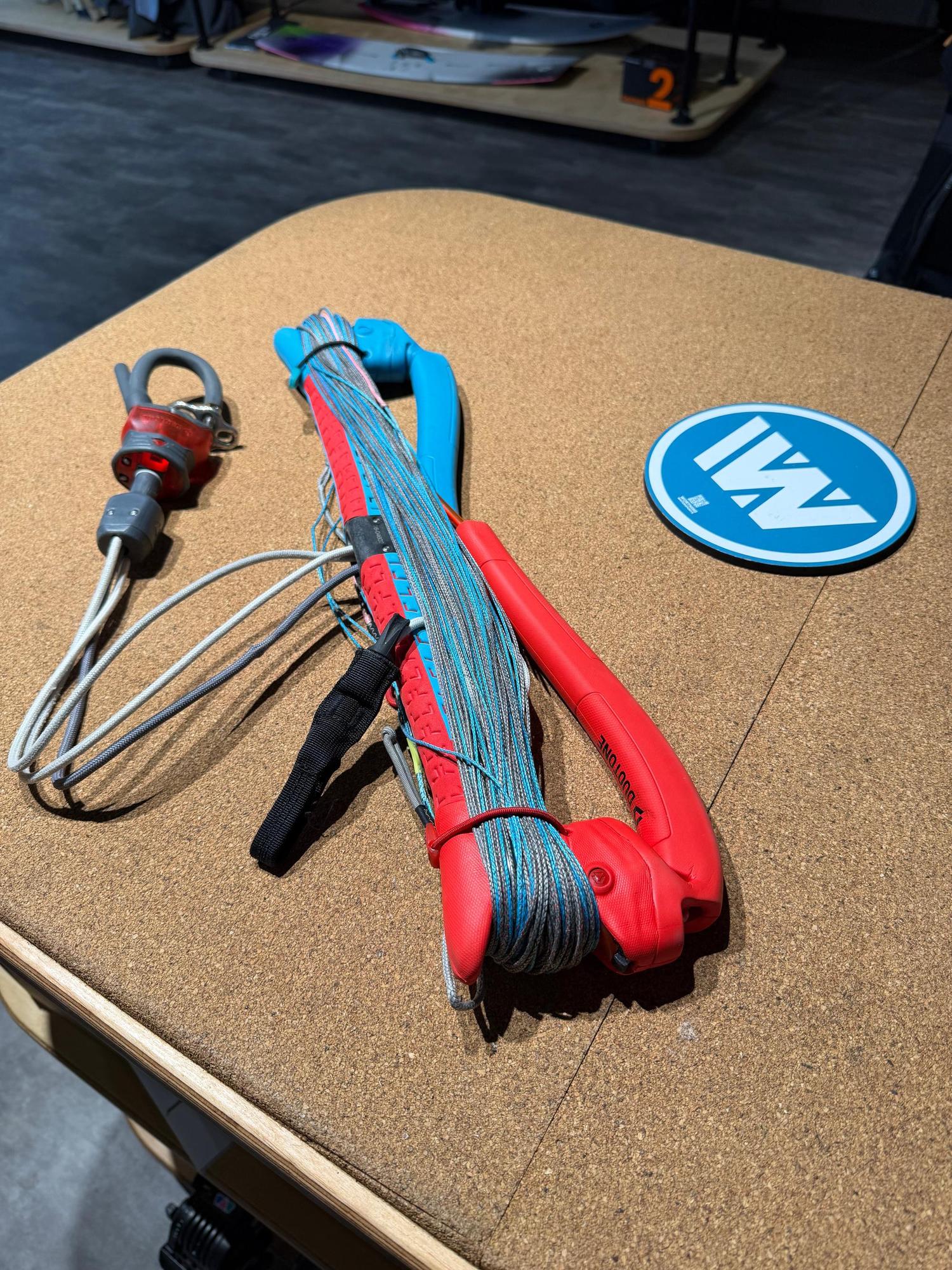 Used Duotone Trust Bar S-M with 22/24m lines, featuring red and blue grips, safety system, and coiled lines on a cork surface.