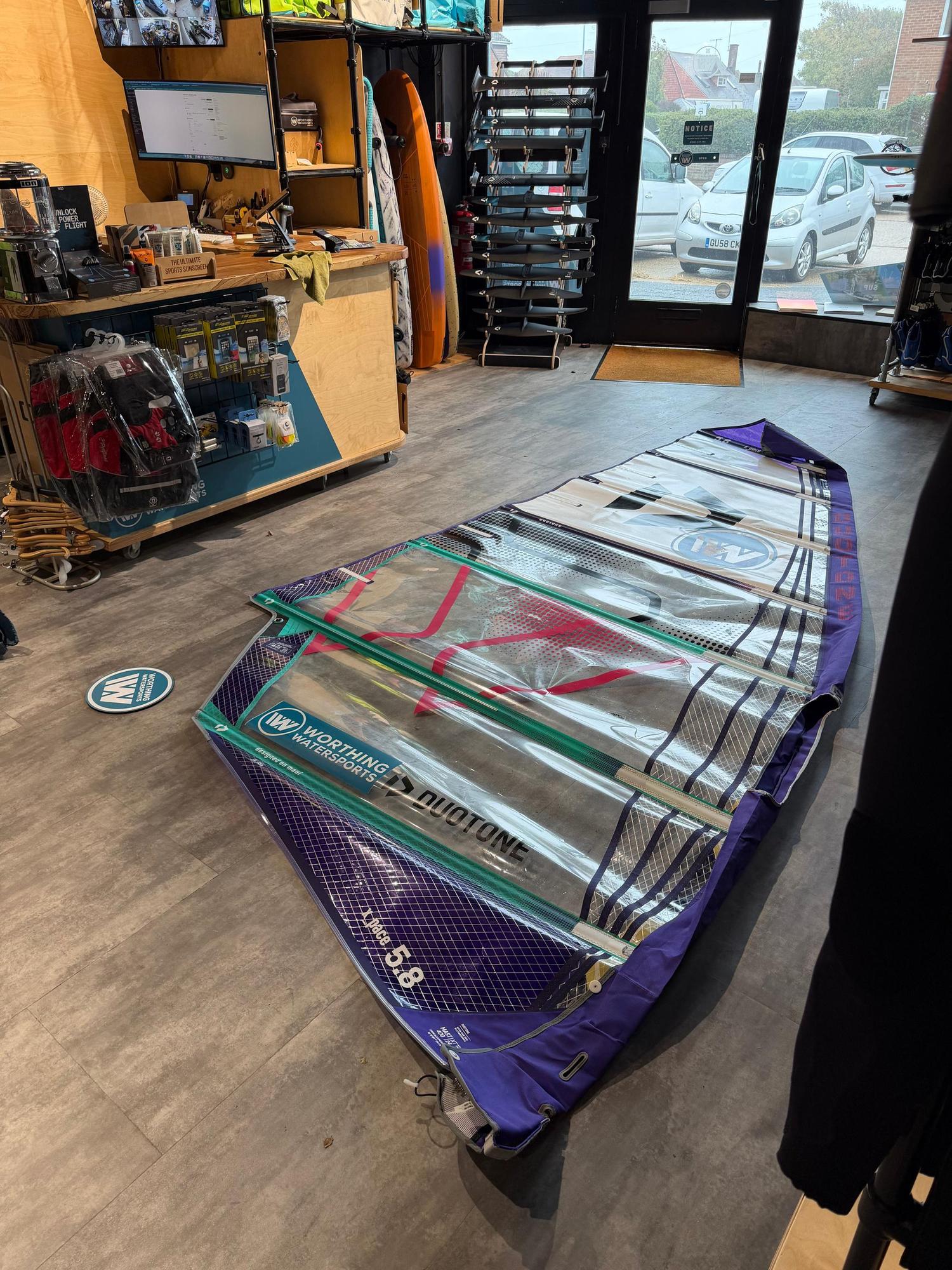 Used Duotone X_Pace 5.8 freeride windsurf sail in purple and white with clear panels laid out on a shop floor.