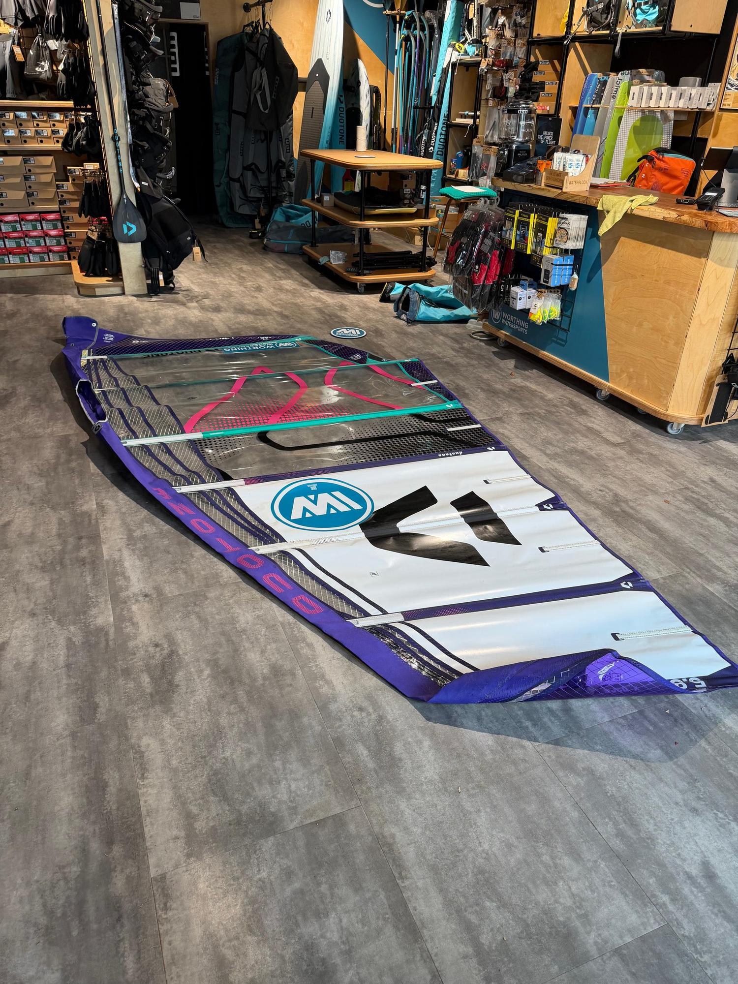 Used Duotone X_Pace 5.8 freerace windsurf sail in purple and white, laid flat on a shop floor with visible sail protectors.