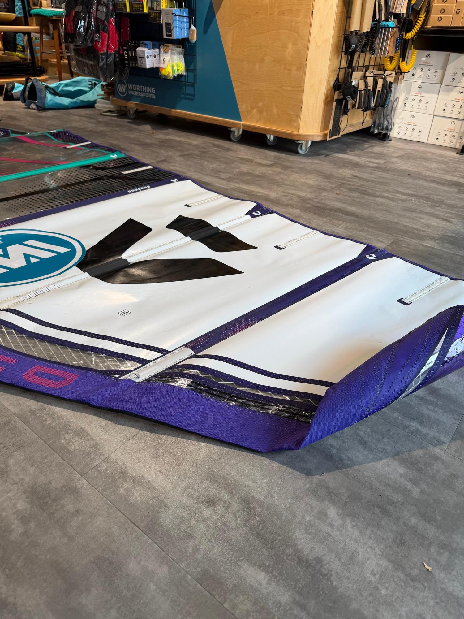 Used Duotone X_Pace 5.8 freerace windsurf sail in white, purple, and teal, laid flat on a shop floor.