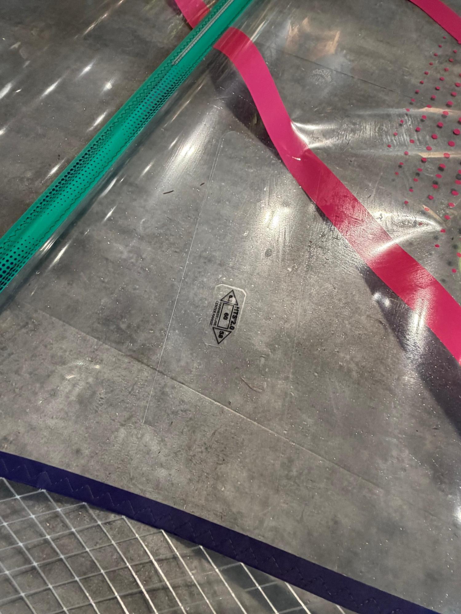 Close-up of a used Duotone X_Pace 5.8 windsurf sail featuring clear monofilm, pink and green trim, and a harness line marker.