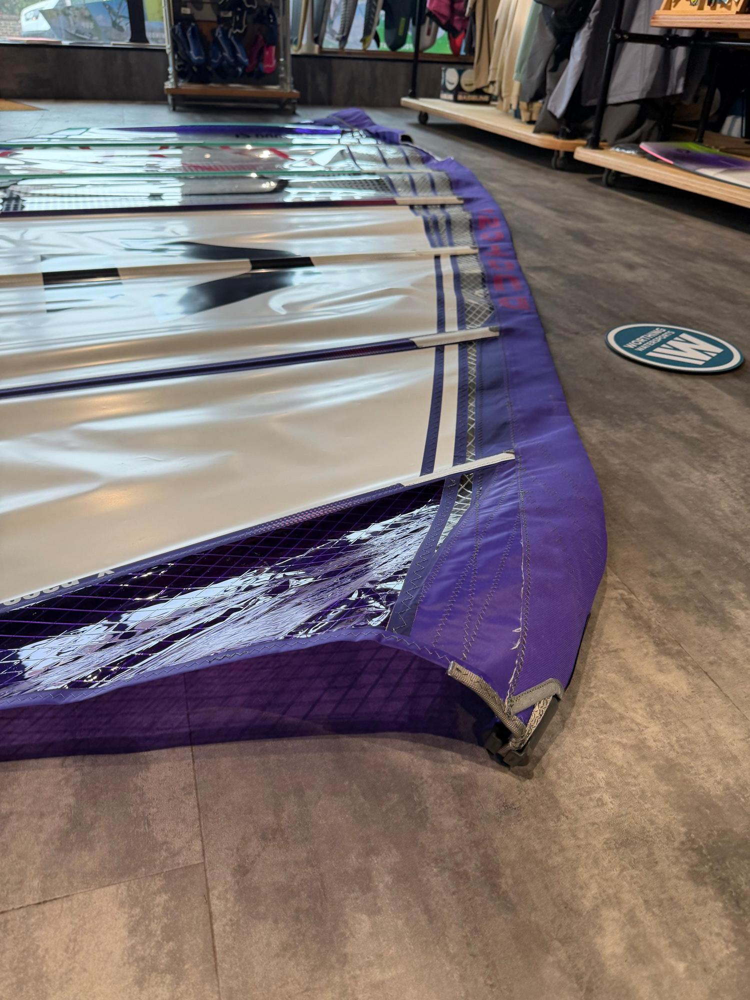 Used Duotone X_Pace 7.3m freerace windsurf sail in purple and white, laid flat on a shop floor.