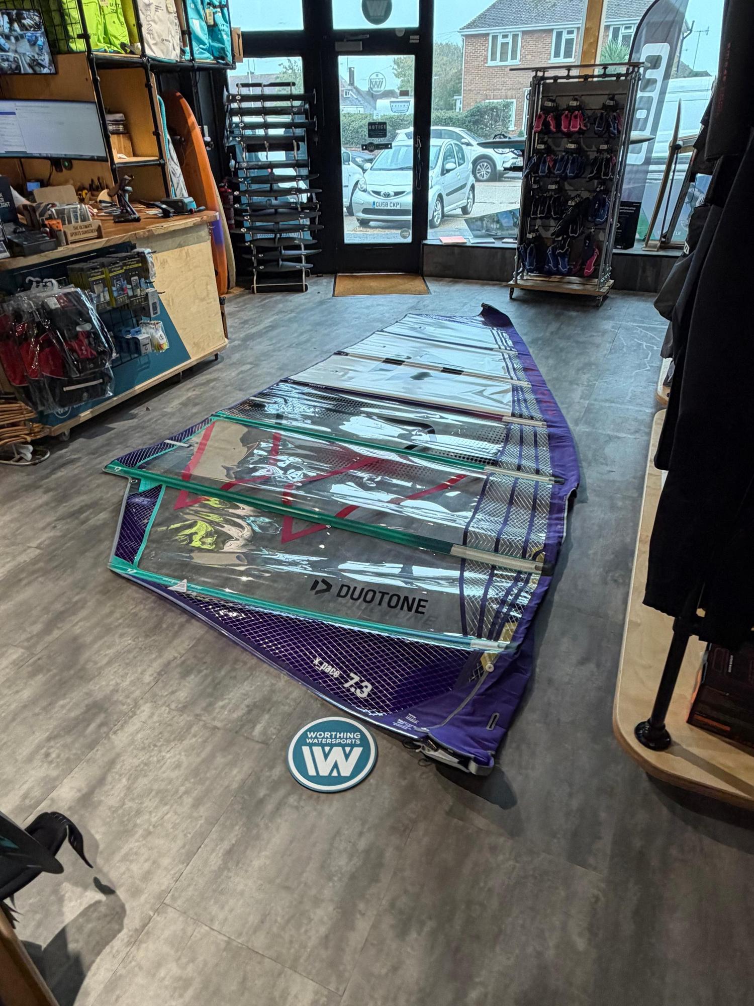Used Duotone X_Pace 7.3m freerace windsurf sail in purple and clear monofilm, laid flat on a shop floor.