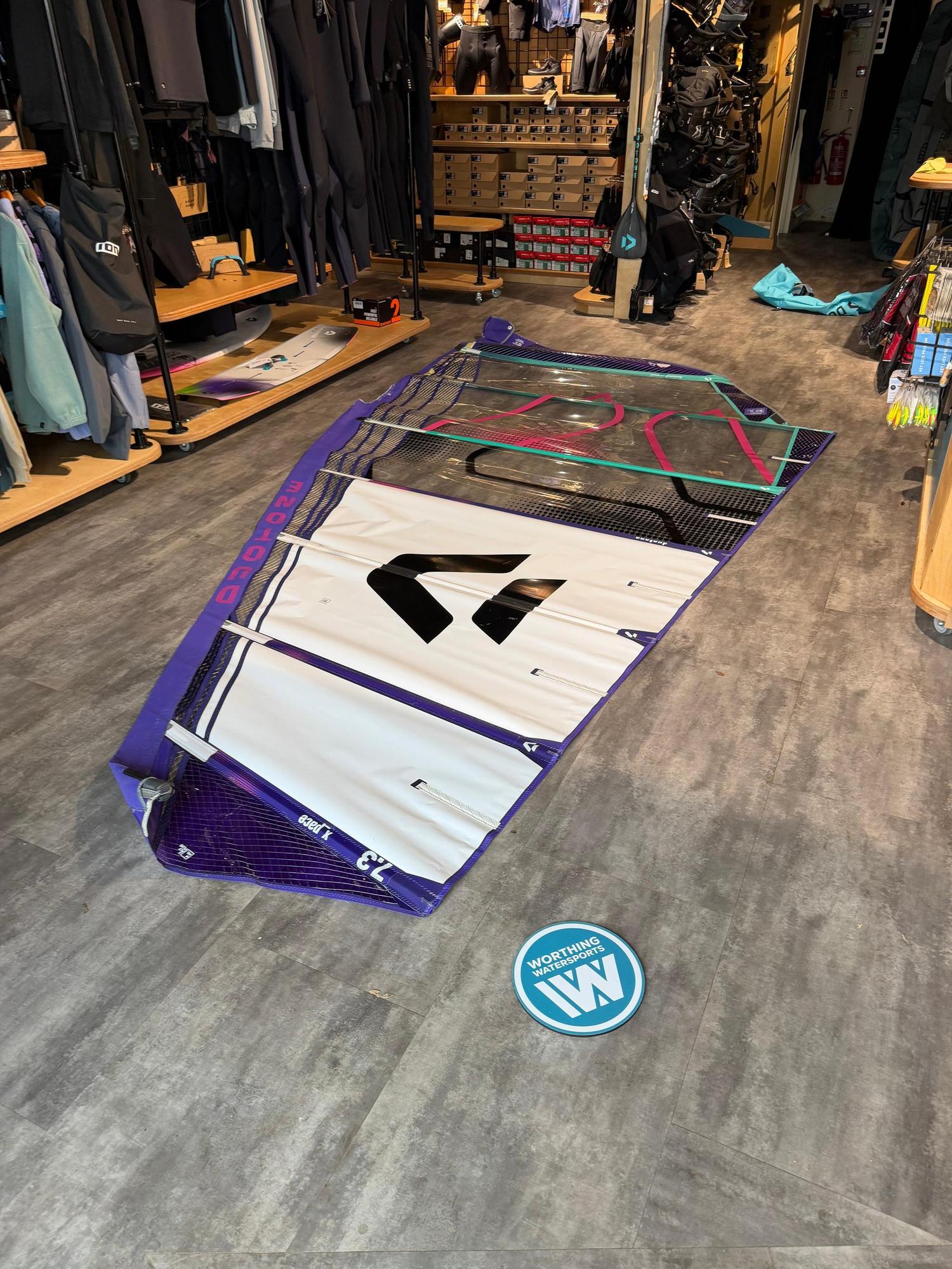 Used Duotone X_Pace 7.3m freerace windsurf sail in white and purple, laid flat on a shop floor.