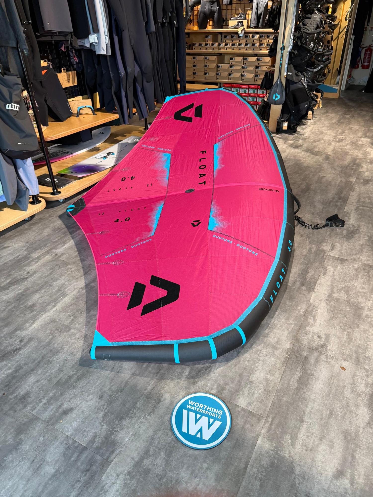 Used Duotone Float 4m wave wing in pink and black, featuring a boom and leash, displayed in a watersports shop.
