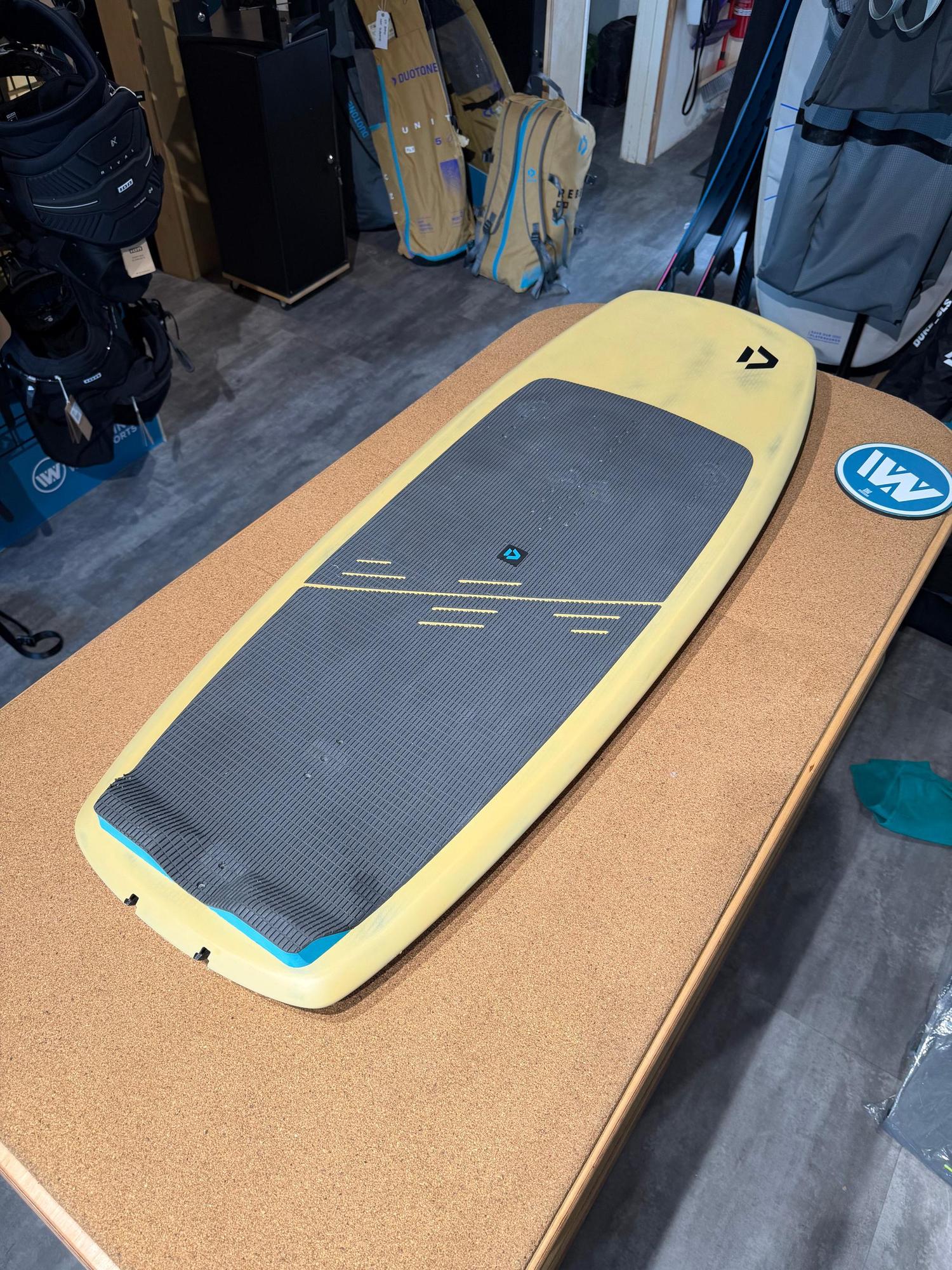 Used Duotone Soar SLS 4'2'' kite foilboard in yellow with a grey deck pad and black Duotone branding on a wooden table.