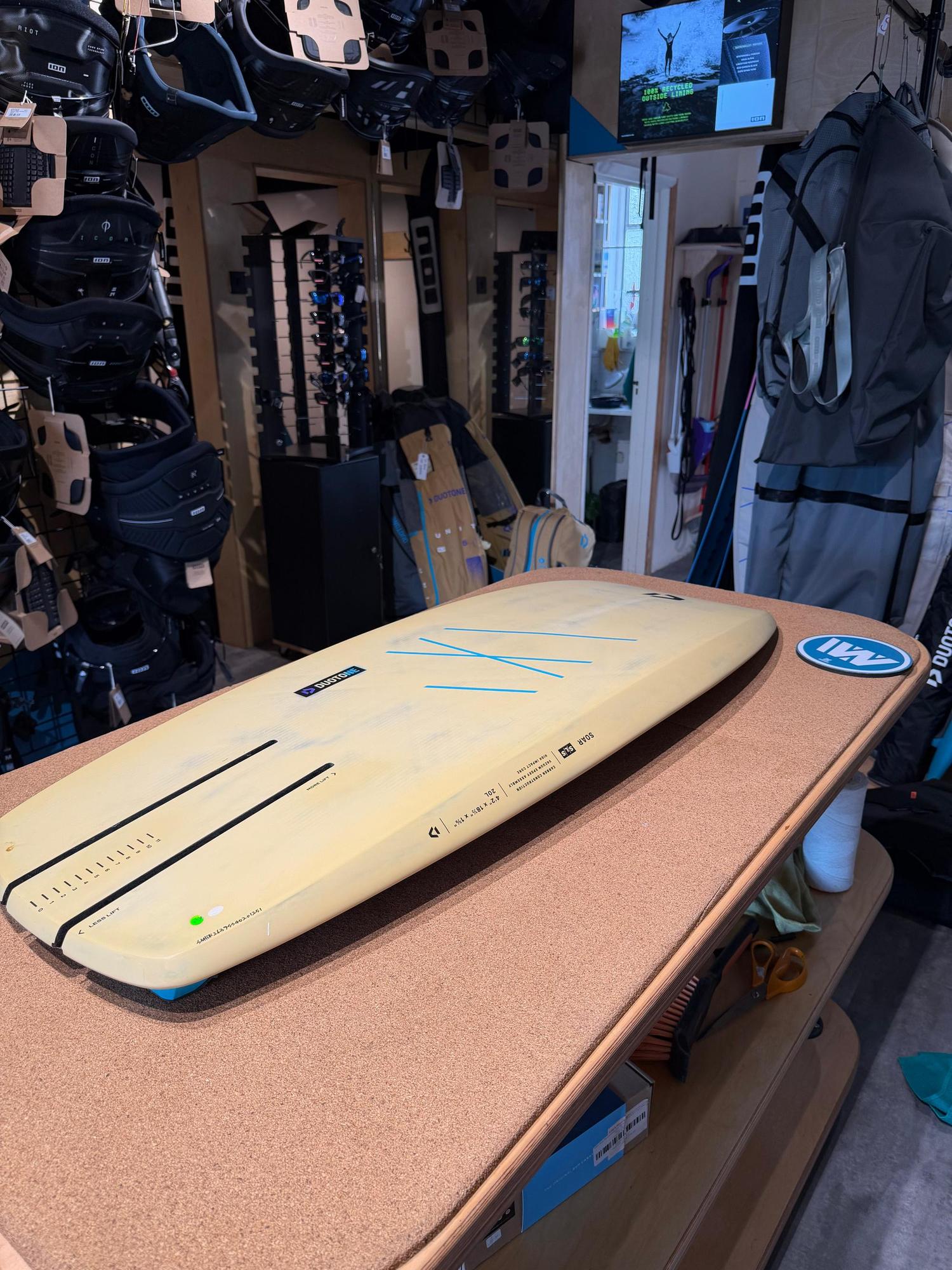 Used Duotone Soar SLS 4'2'' carbon kite foilboard in cream with blue detailing, displayed on a shop counter.