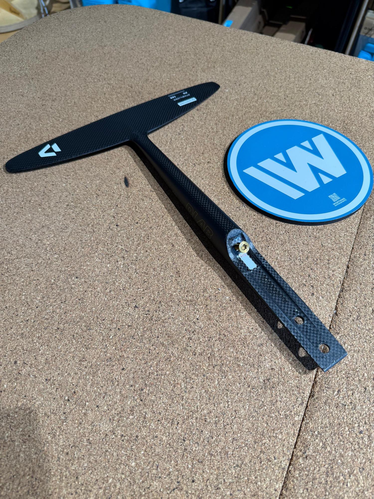 Black carbon fibre Duotone Monobloc-Tail PX 40/145 stabiliser wing with integrated fuselage on a cork surface.
