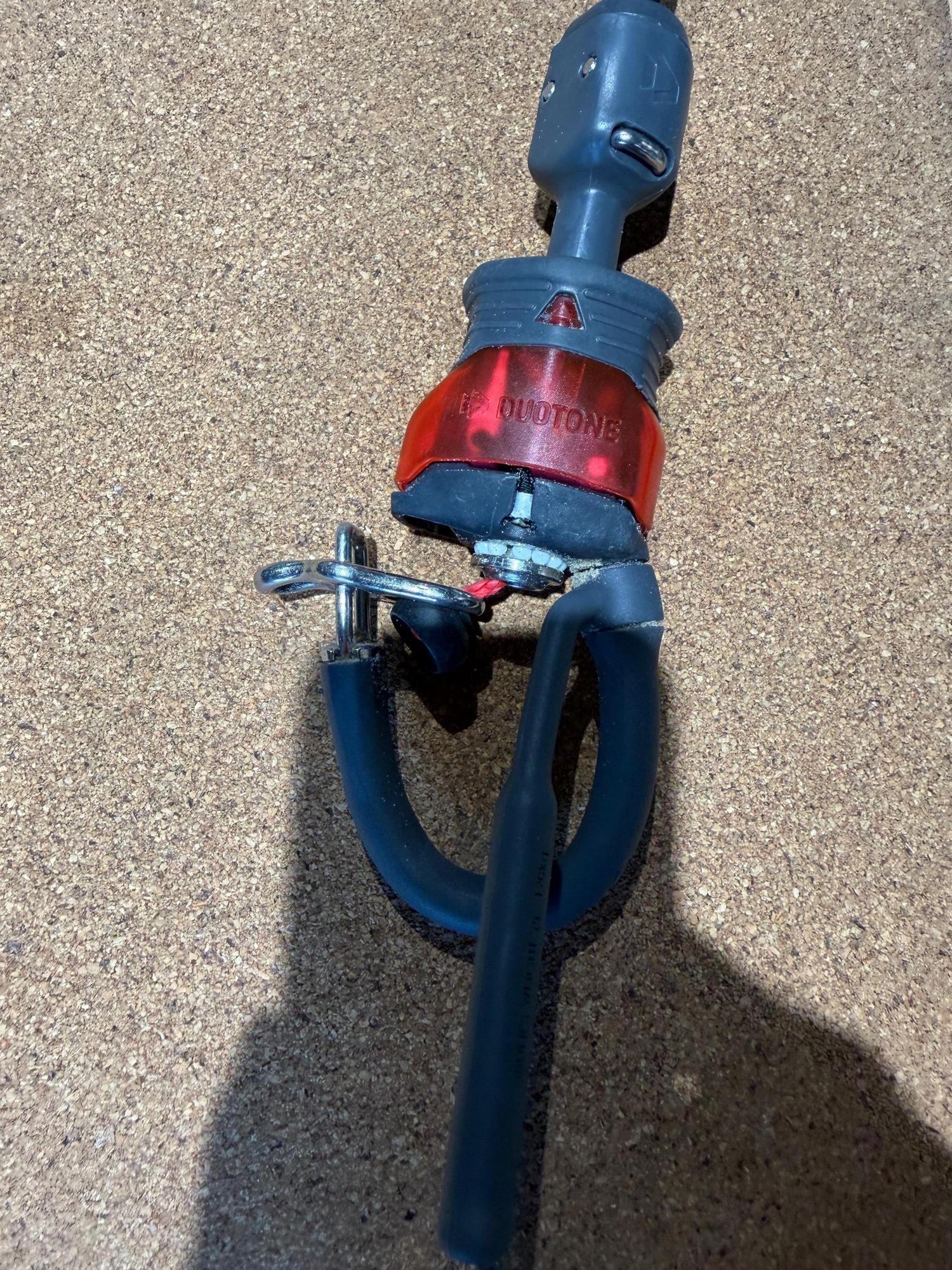 Used Duotone Click Bar 2026 S size chicken loop with red safety release mechanism and metal hardware on a cork background.