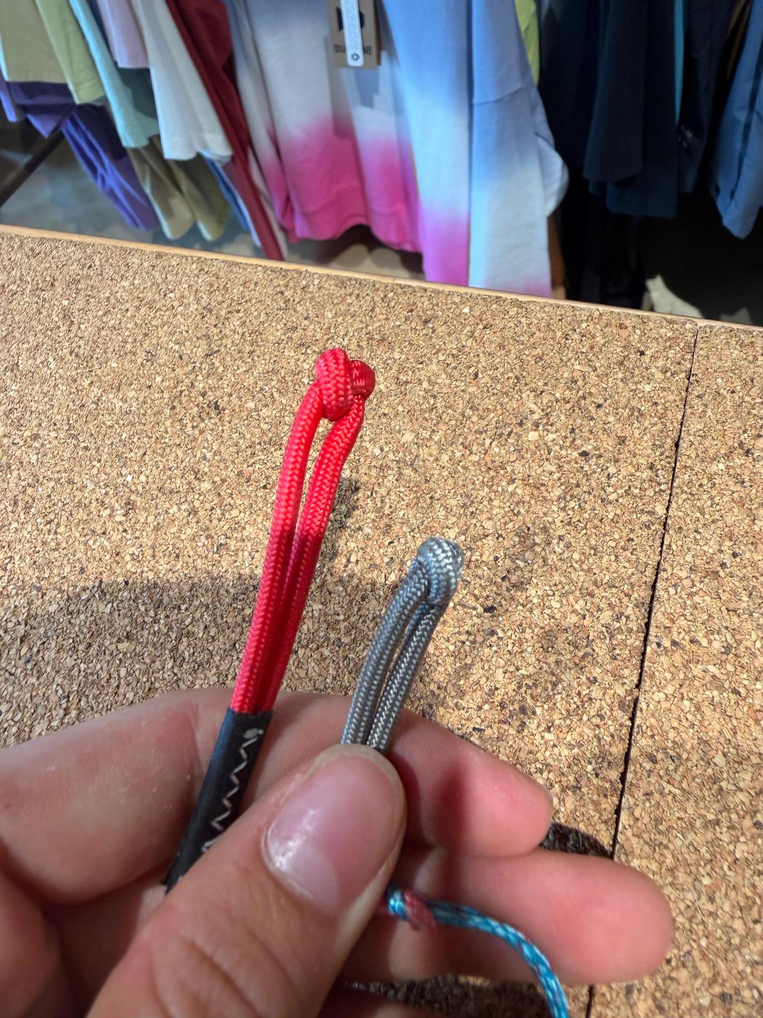 Hand holding red and grey pigtail connectors for a Duotone Click Bar on a cork surface.