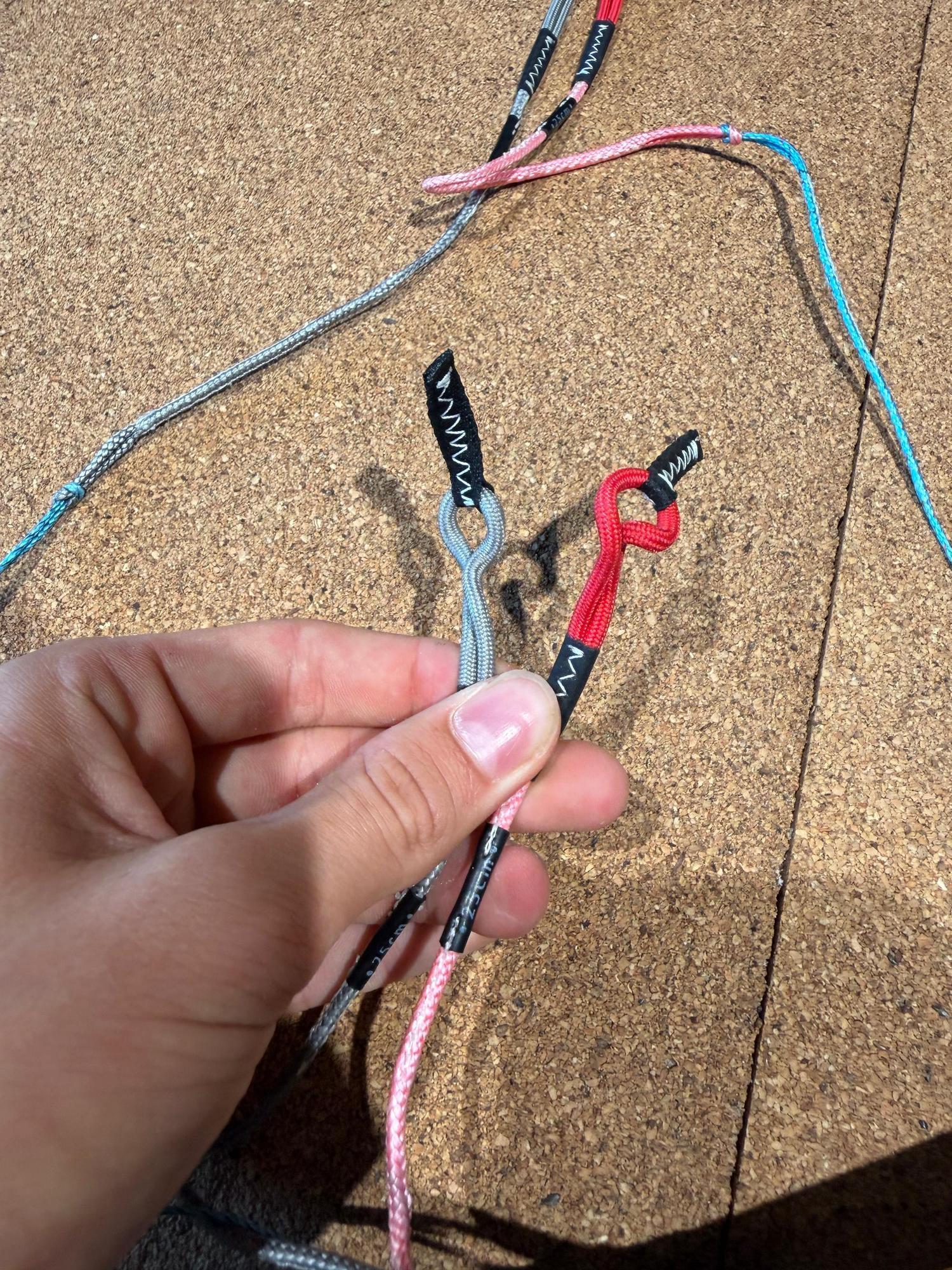 Hand holding Duotone Click Bar 2026 kiteboarding pigtail lines with grey, red, and pink colour-coded connectors.