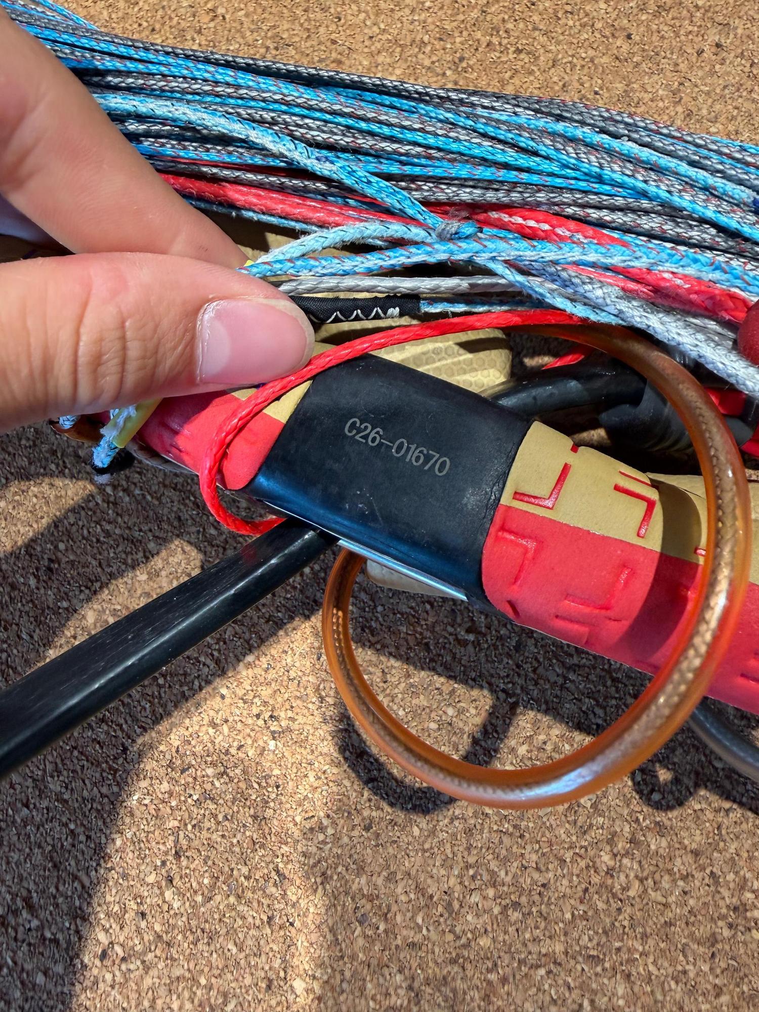 Hand holding a used Duotone Click Bar 2026 with red and tan grip, showing the safety loop and blue and red kite lines.