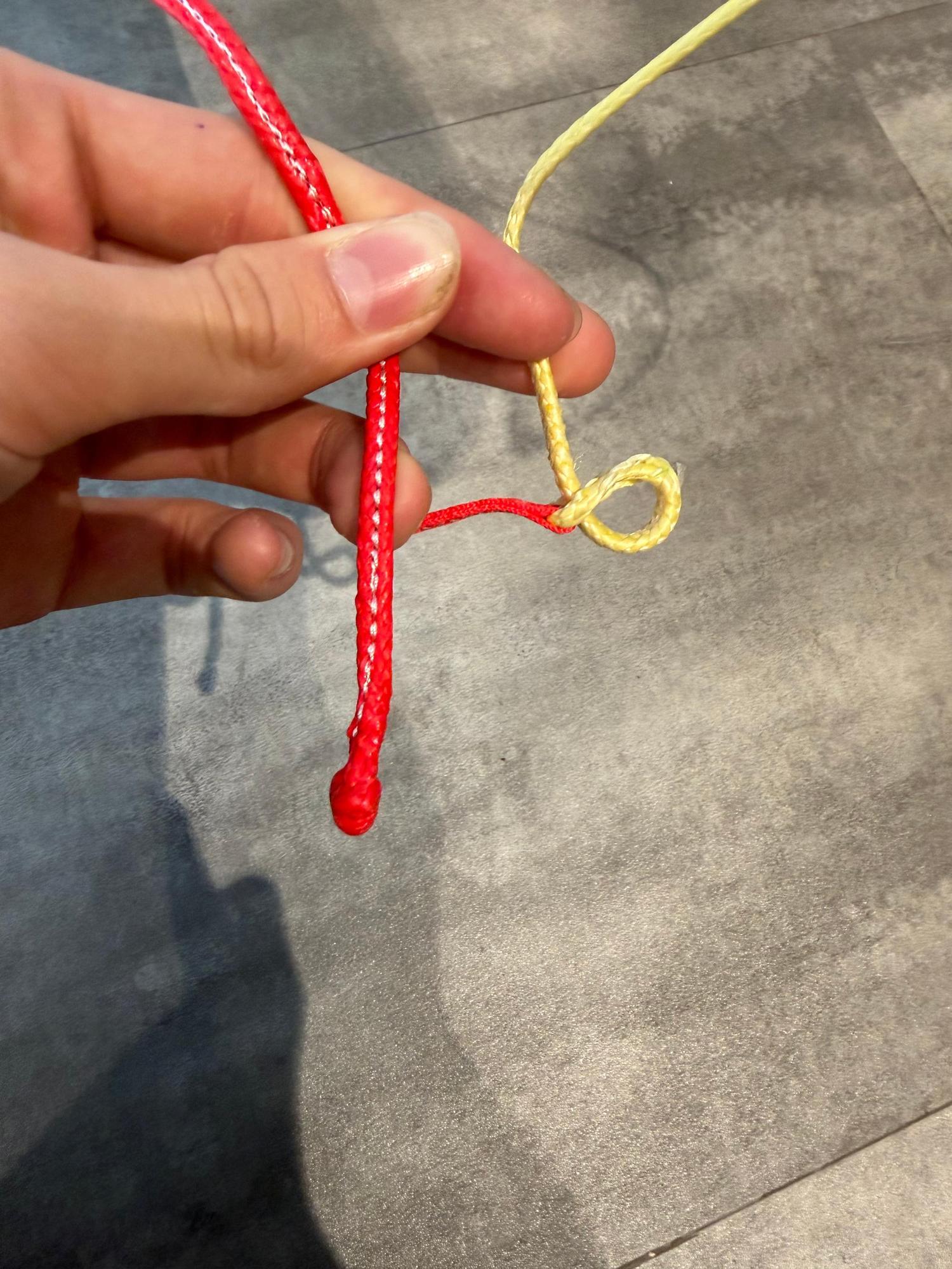 Hand holding red and yellow braided kite lines with a loop knot for a Duotone Rebel SLS Concept Blue kite.