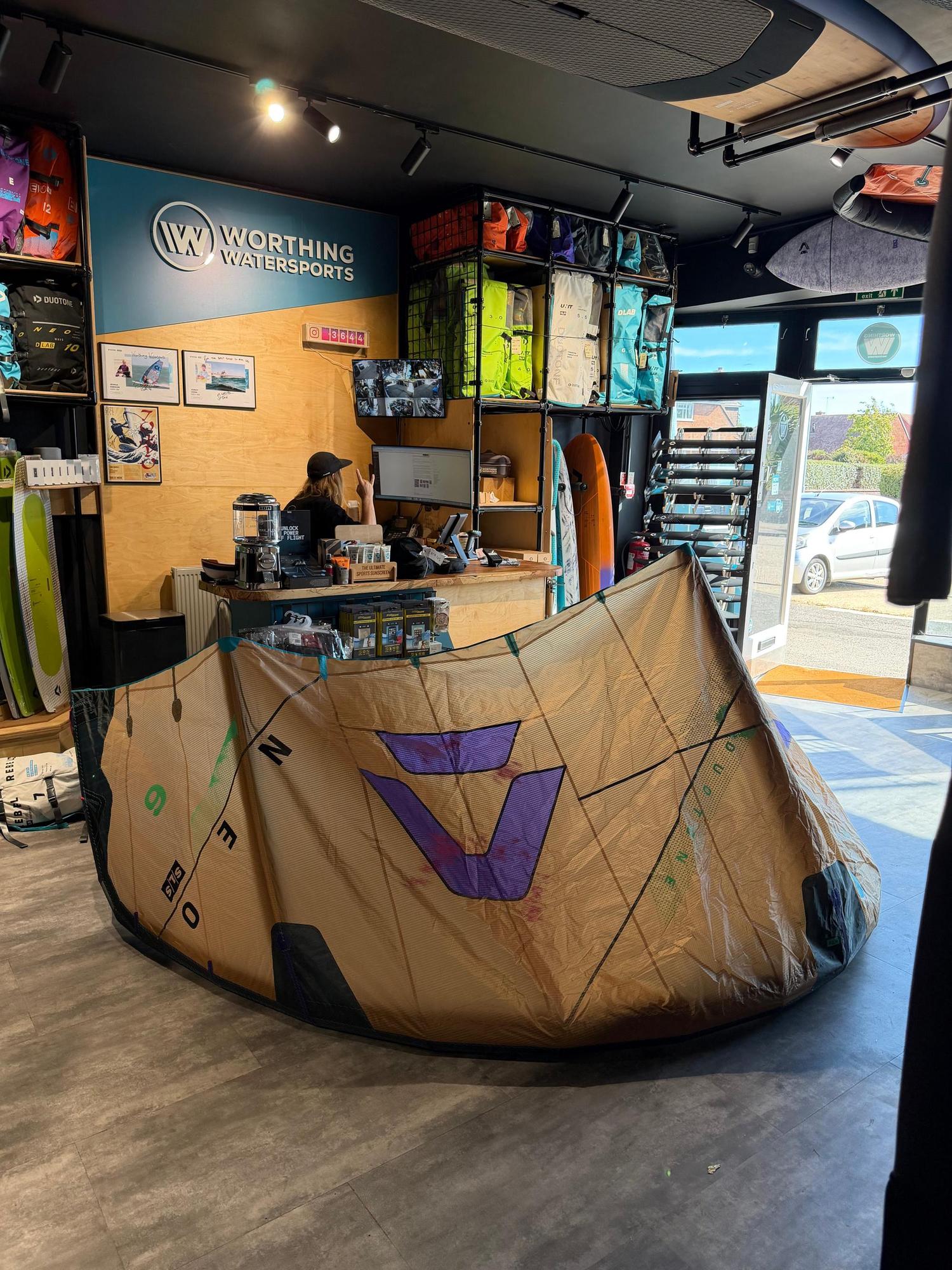 Used 6m Duotone Neo SLS wave kite in tan and purple, displayed on a shop floor with visible branding and strut construction.