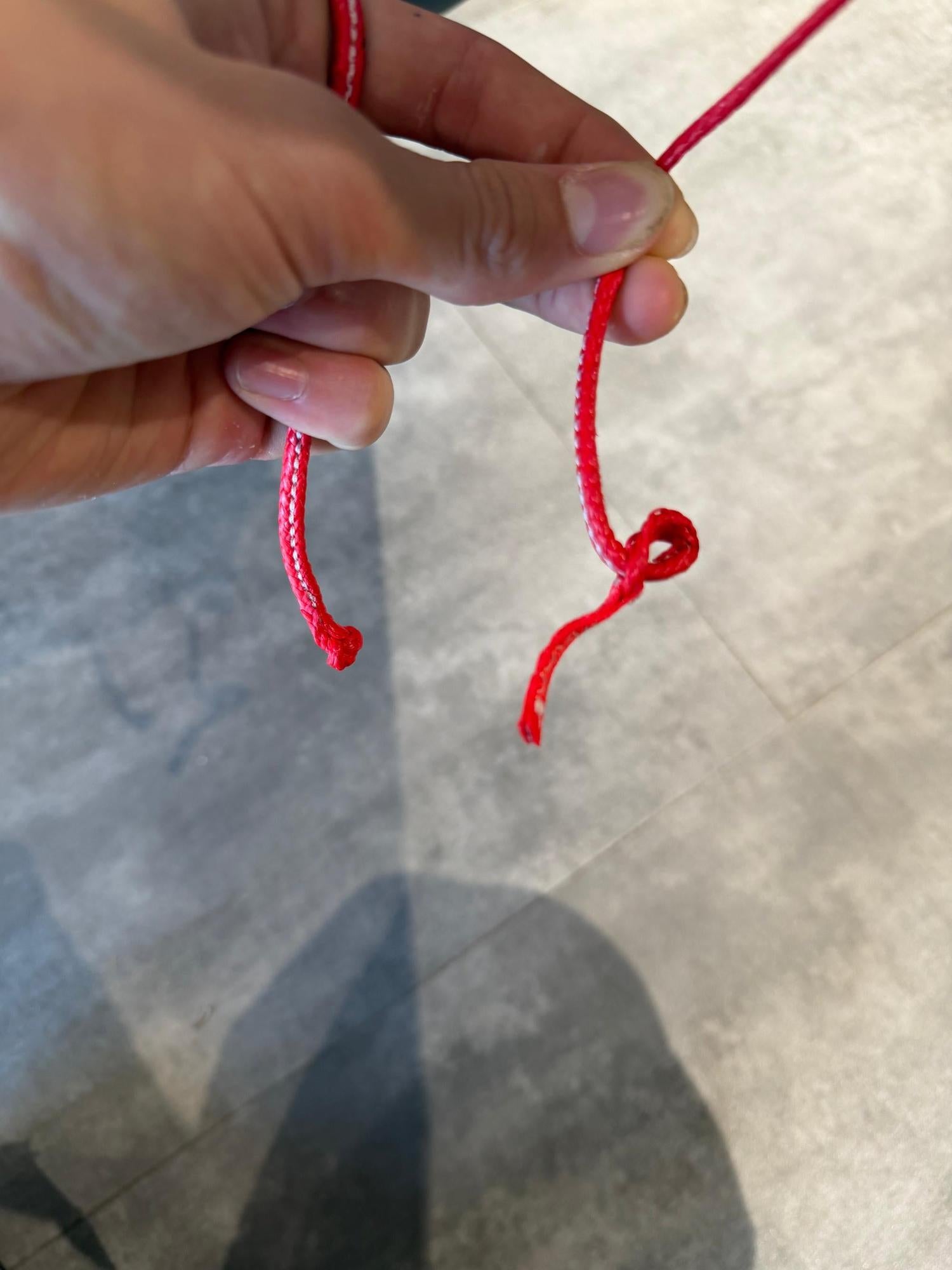 Hand holding a bright red pigtail line from a Duotone Neo SLS wave kite, showing durable cord construction.