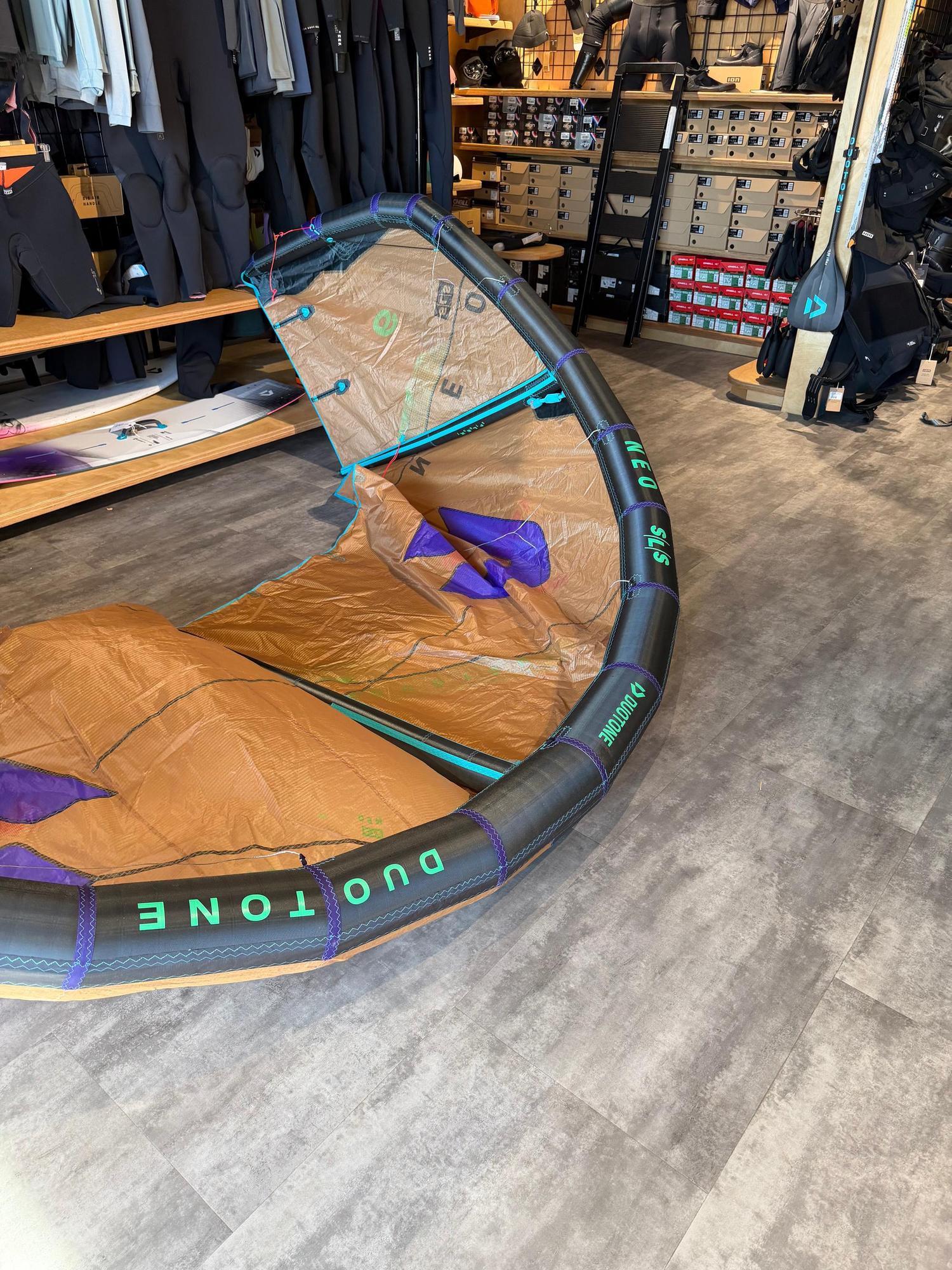 Used 6m Duotone Neo SLS wave kite in brown and black with green branding, displayed on a shop floor.