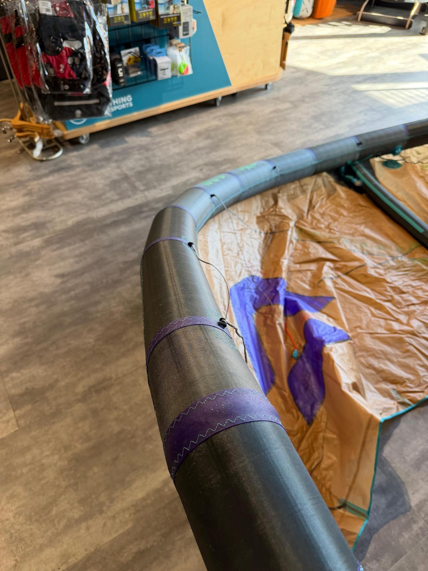 Used 6m Duotone Neo SLS wave kite featuring a black leading edge with purple detailing and a tan canopy in a retail shop.