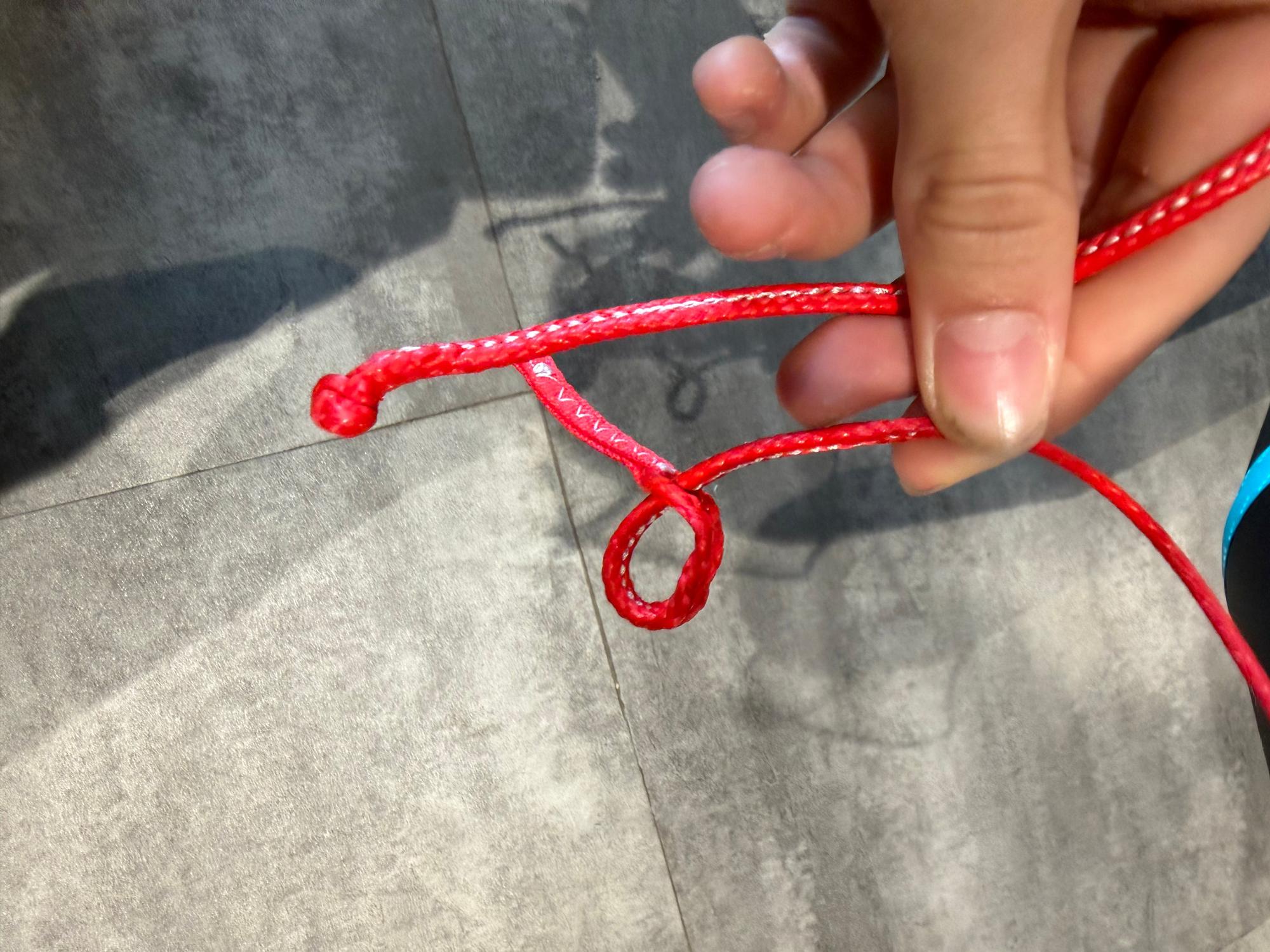 Hand holding a bright red pigtail connector line for a Duotone Rebel SLS kite, showing a knotted loop end.