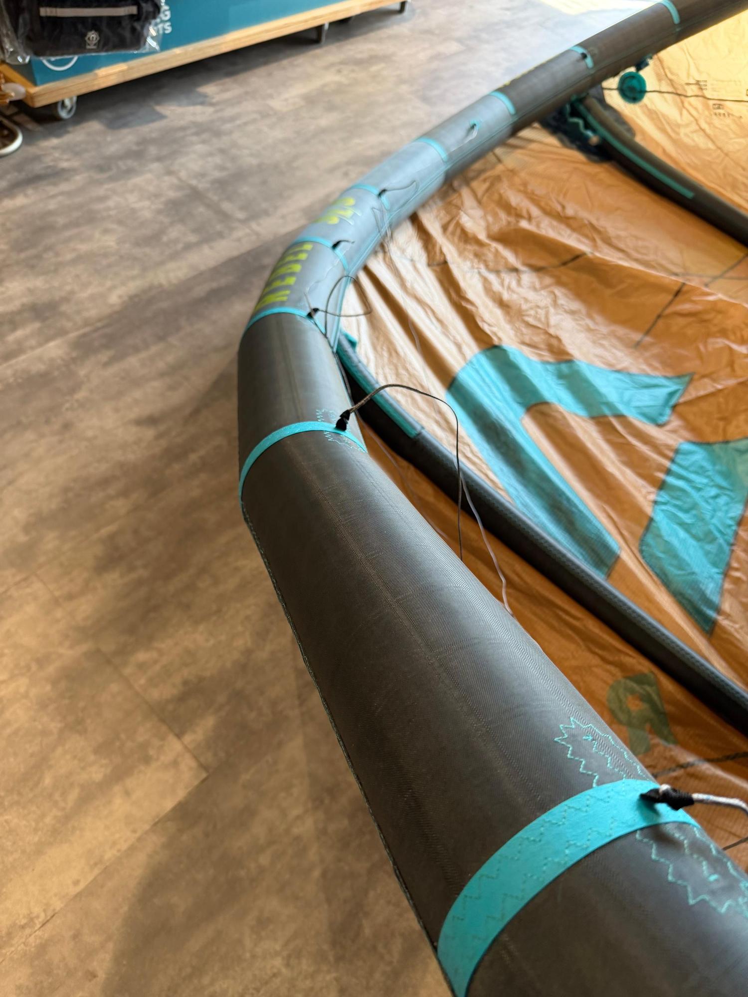 Used 8m Duotone Rebel SLS 2026 kite with grey leading edge, teal accents, and crispy tan canopy fabric on a shop floor.