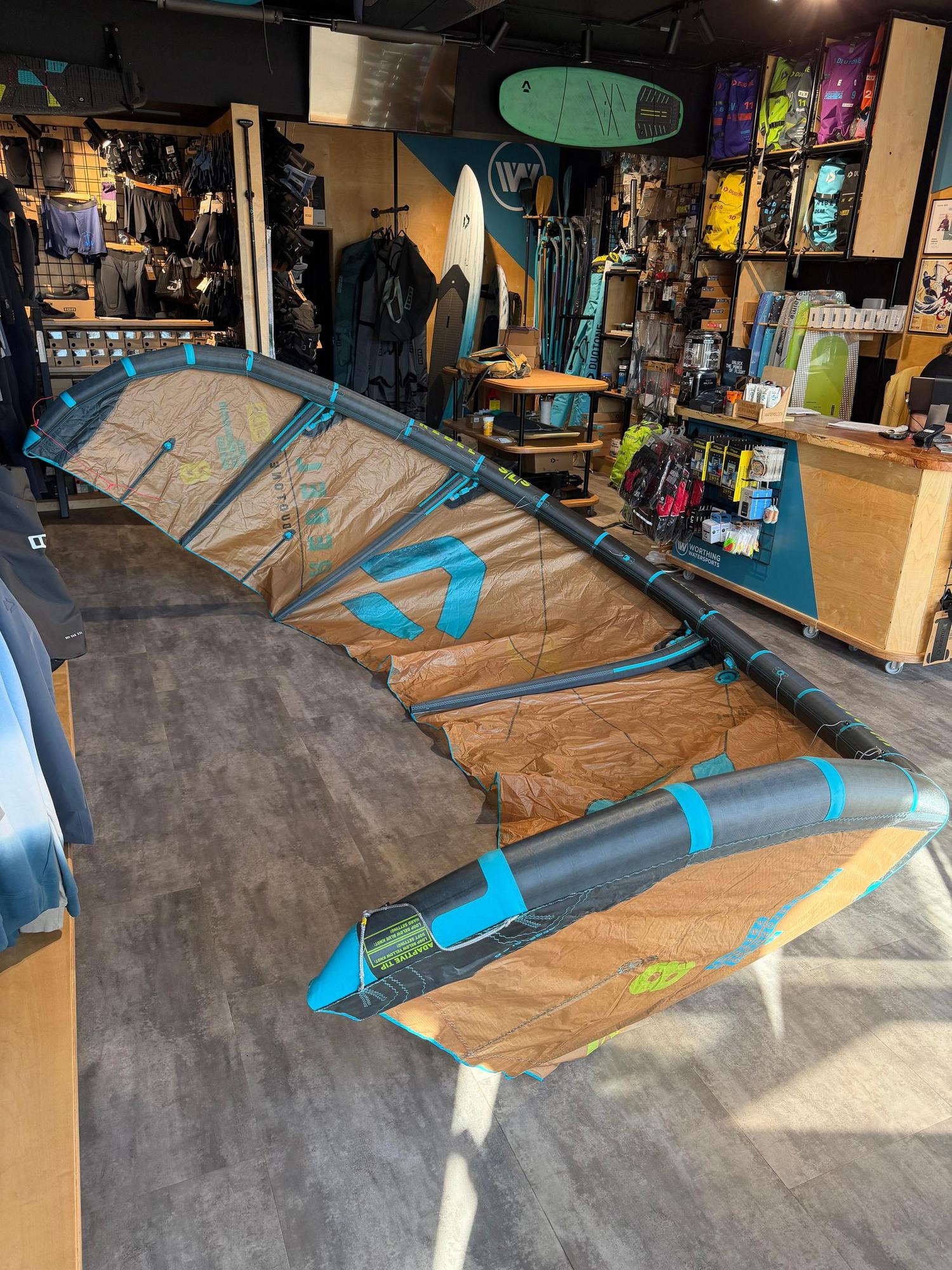 Used 8m Duotone Rebel SLS 2026 big air kite in tan and black with teal accents, displayed in a retail shop.