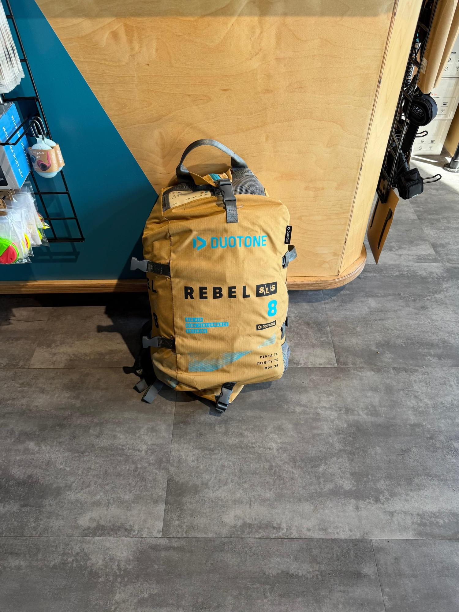 Tan Duotone Rebel SLS 8m kite bag with blue branding and Penta TX material details, standing on a grey floor.