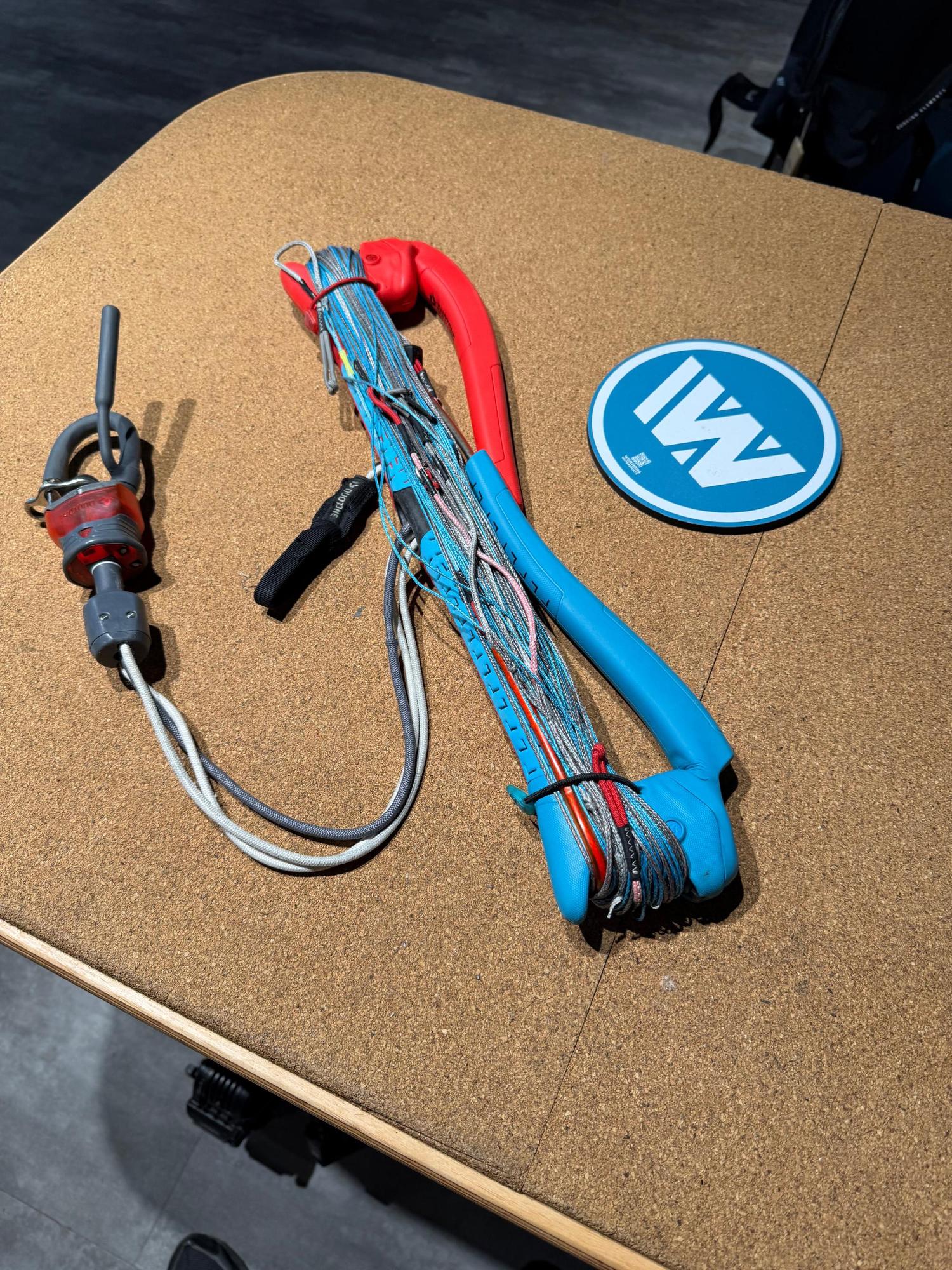 Used Duotone Trust Bar S-M 22/24 with red and blue grip, safety system, and coiled lines on a cork table surface.