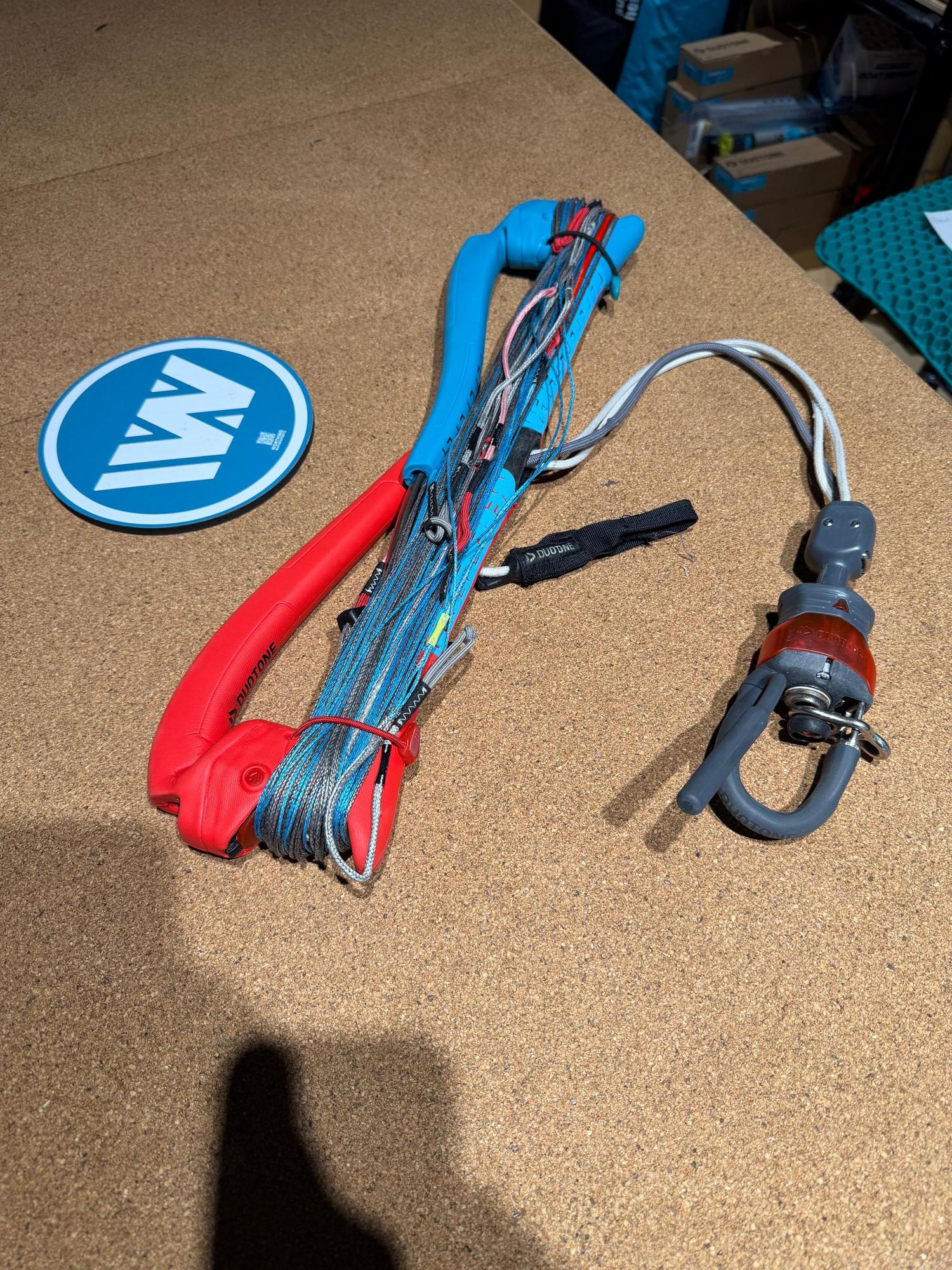 Used Duotone Trust Bar S-M 22/24 with red and blue grip, wound lines, and Click-In safety system on a cork surface.