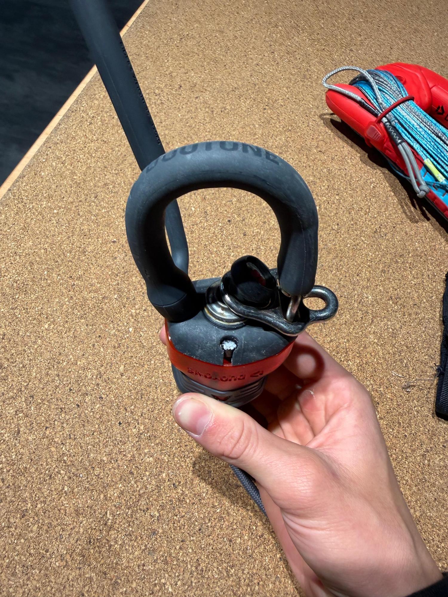 Hand holding a used Duotone Trust Bar featuring a black chicken loop and red Click-In safety system on a cork surface.