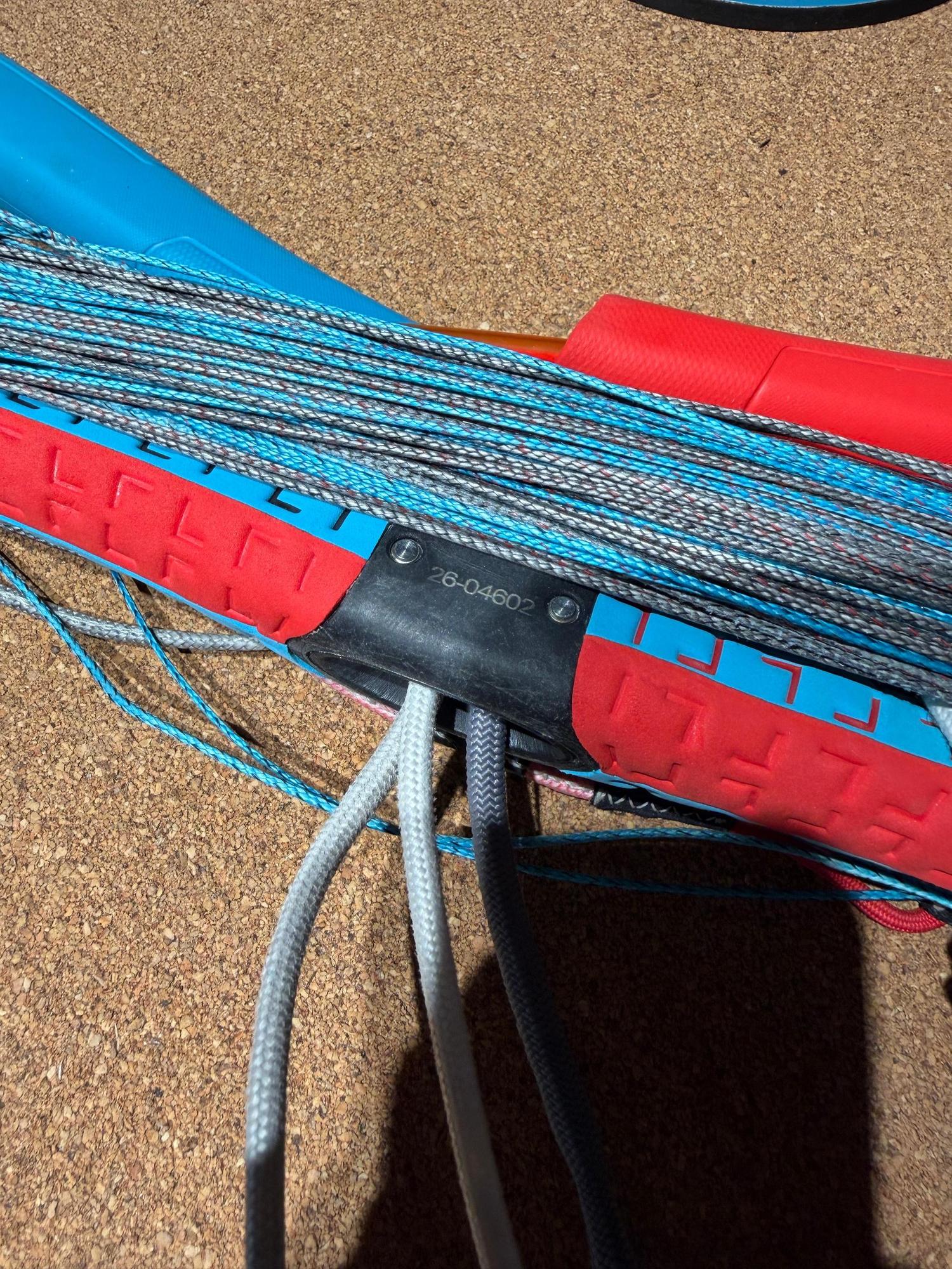 Used Duotone Trust Bar S-M with red and blue textured grip, coiled lines, and central black housing on a cork surface.