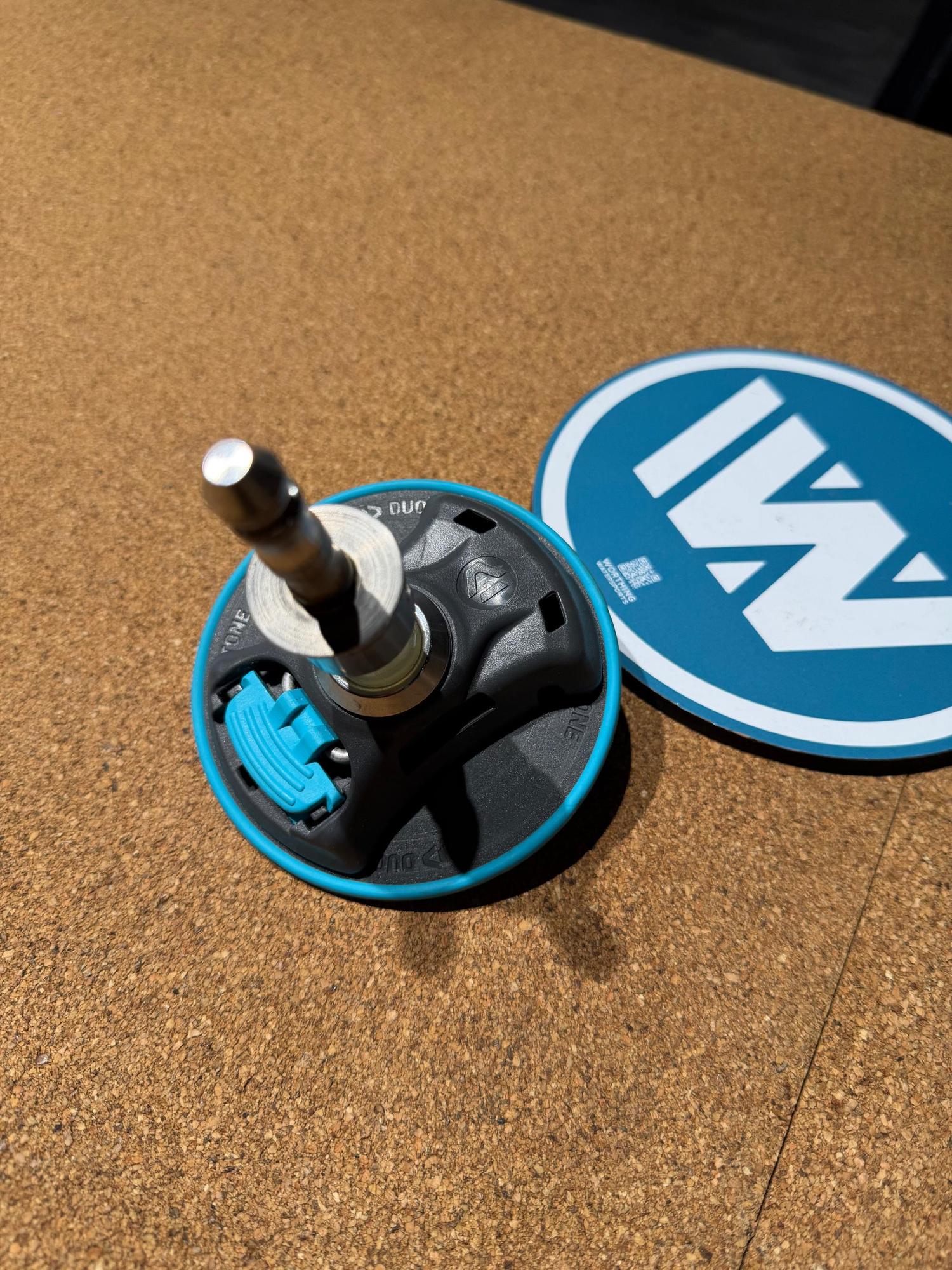 Used Duotone iBase 2.0 windsurfing mast base with blue trim and metal tendon on a cork surface.