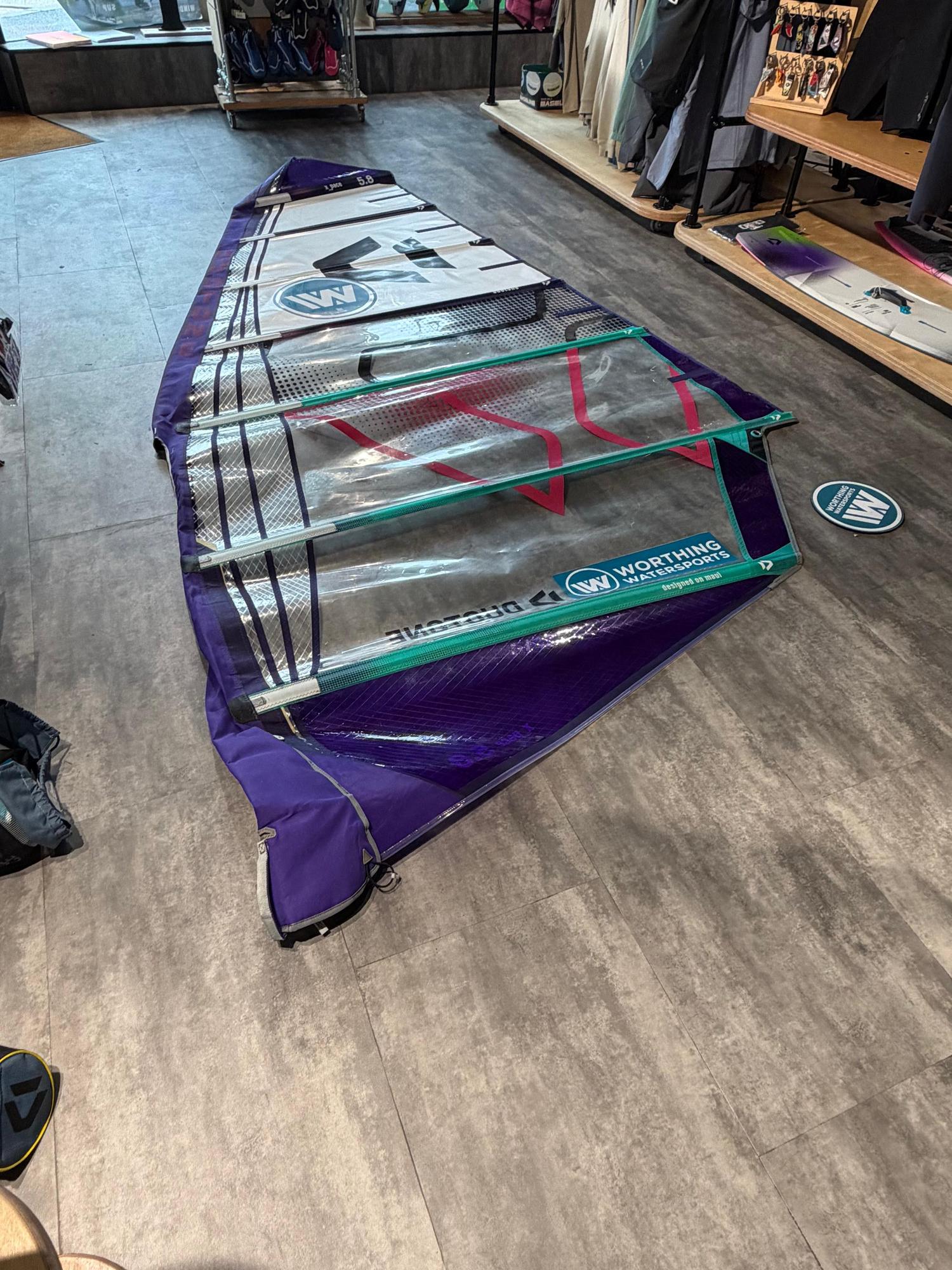 Used Duotone X_Pace 5.8 freerace windsurf sail in purple and clear monofilm with protective panels laid on a shop floor.