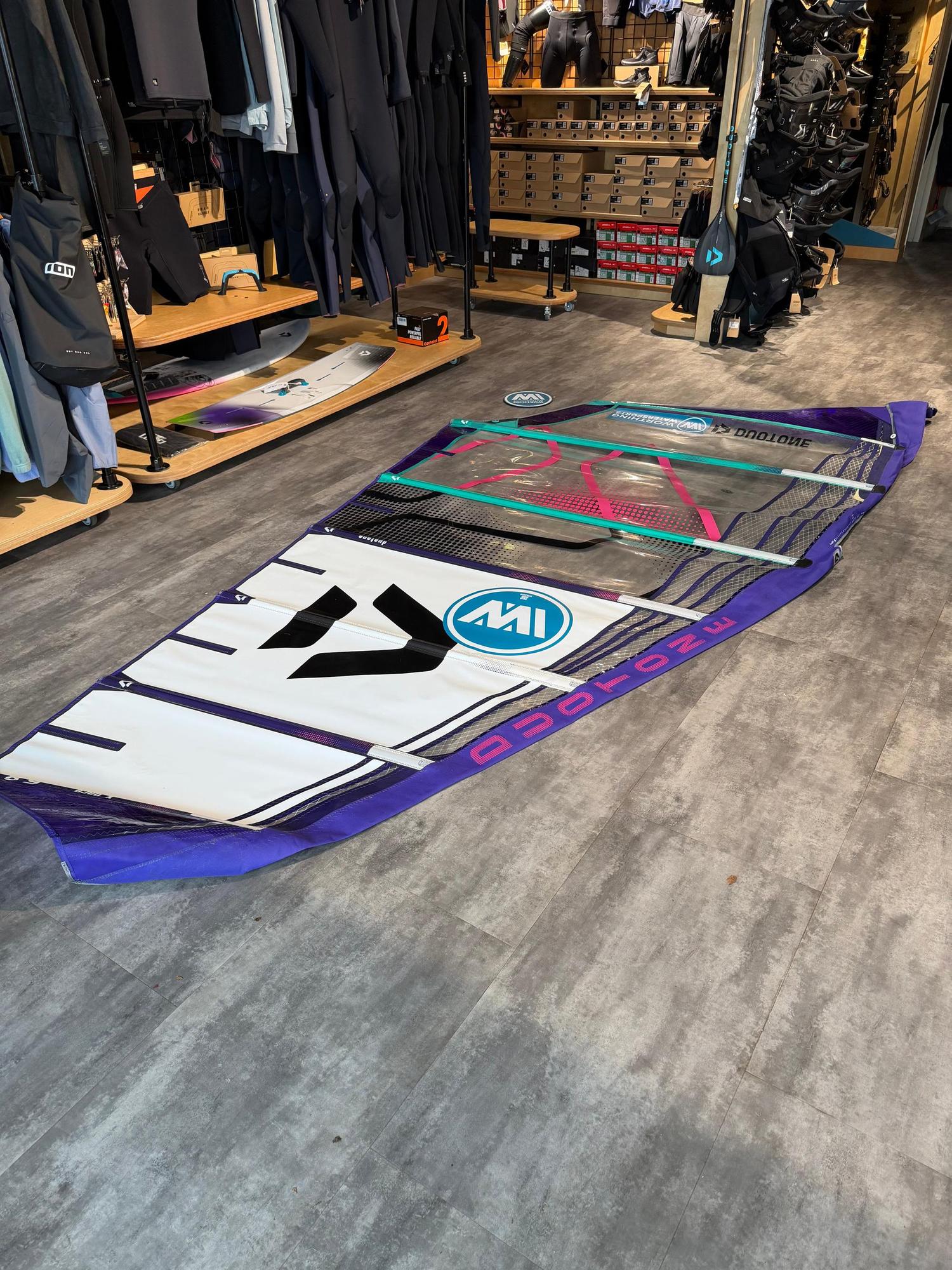 Used Duotone X_Pace 5.8 freerace windsurf sail in purple and white, laid flat on a shop floor with visible sail protectors.