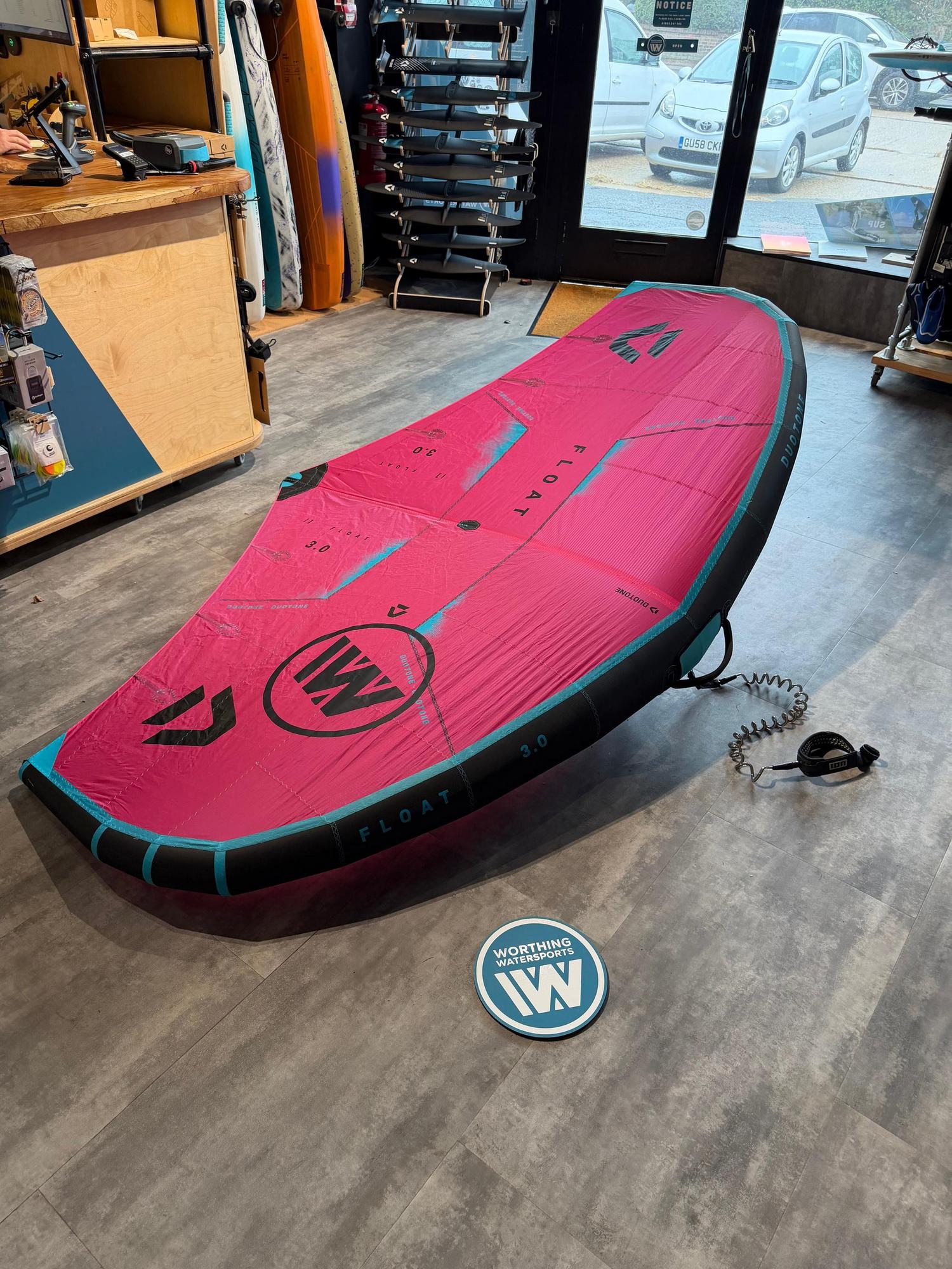 Used Duotone Float 3m wave wing in pink and black, featuring a boom and laid flat on a shop floor.