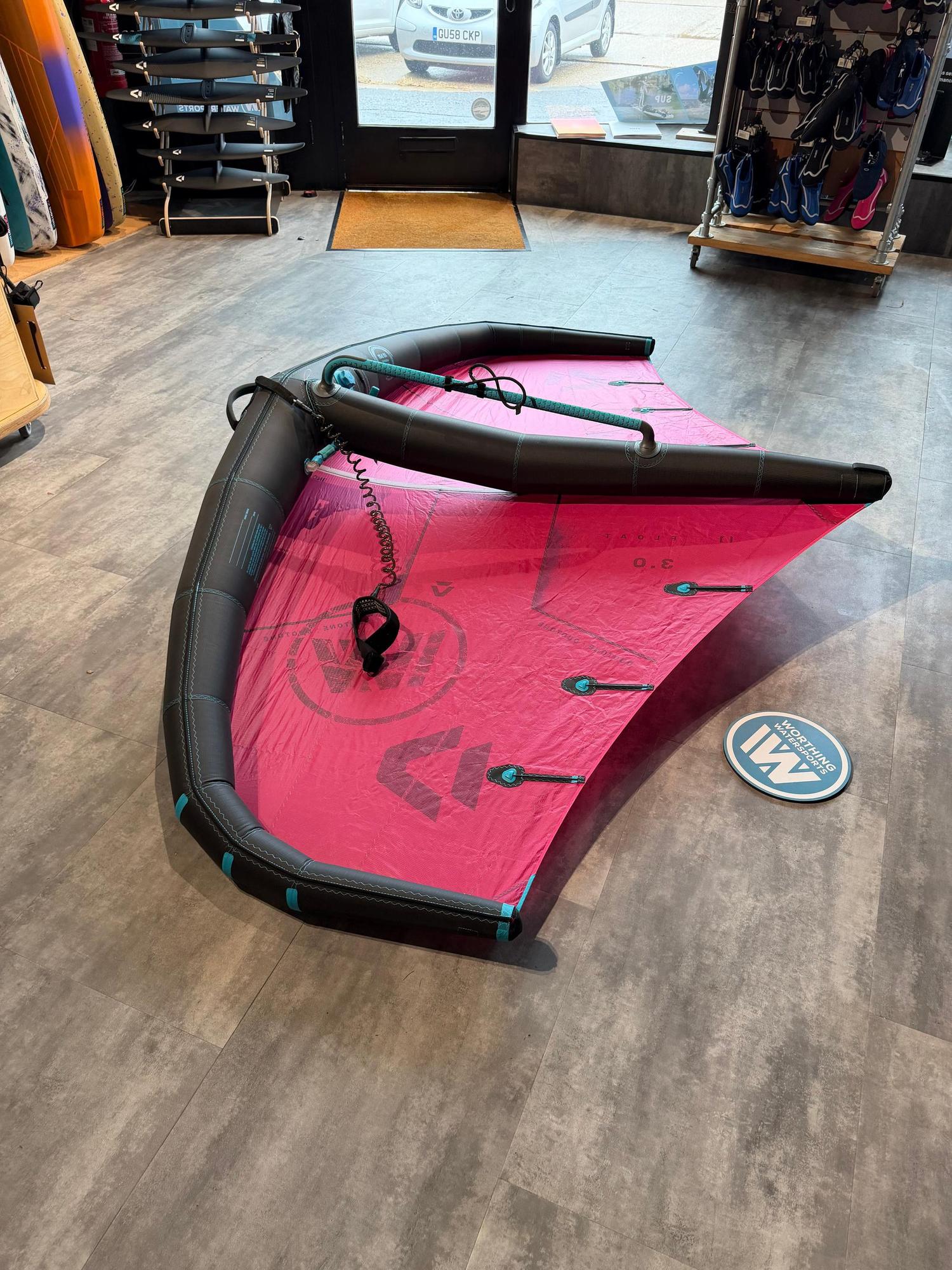 Used Duotone Float 3m wave wing in pink and black with an integrated boom, displayed on a shop floor.
