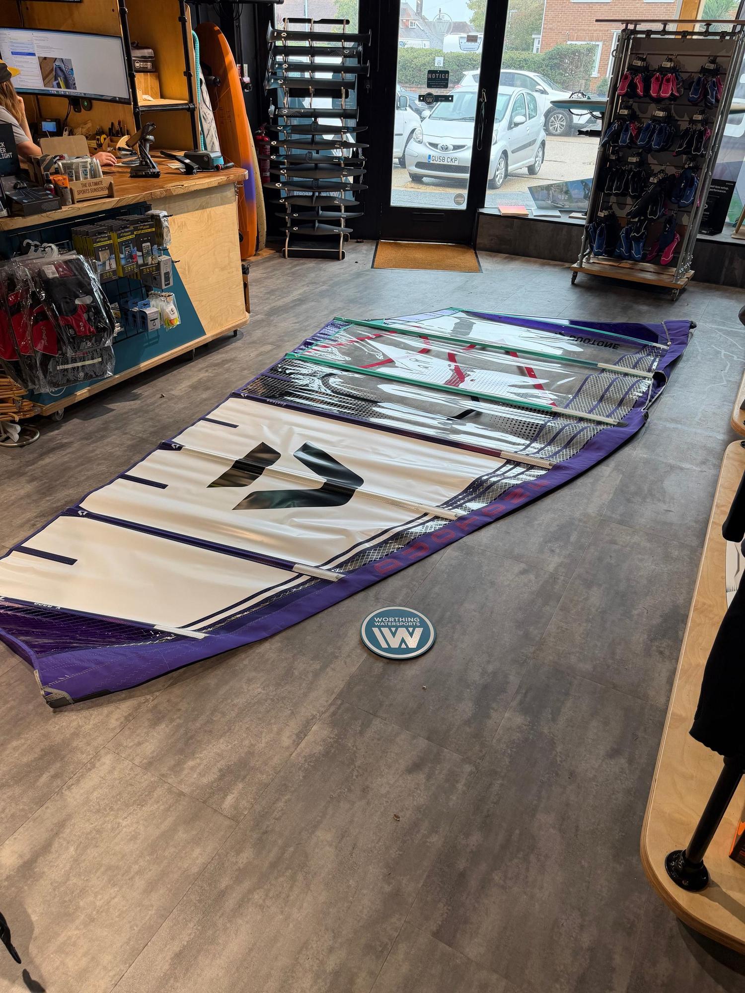 Used Duotone X_Pace 7.3m freerace windsurf sail in white and purple, laid flat on a shop floor.
