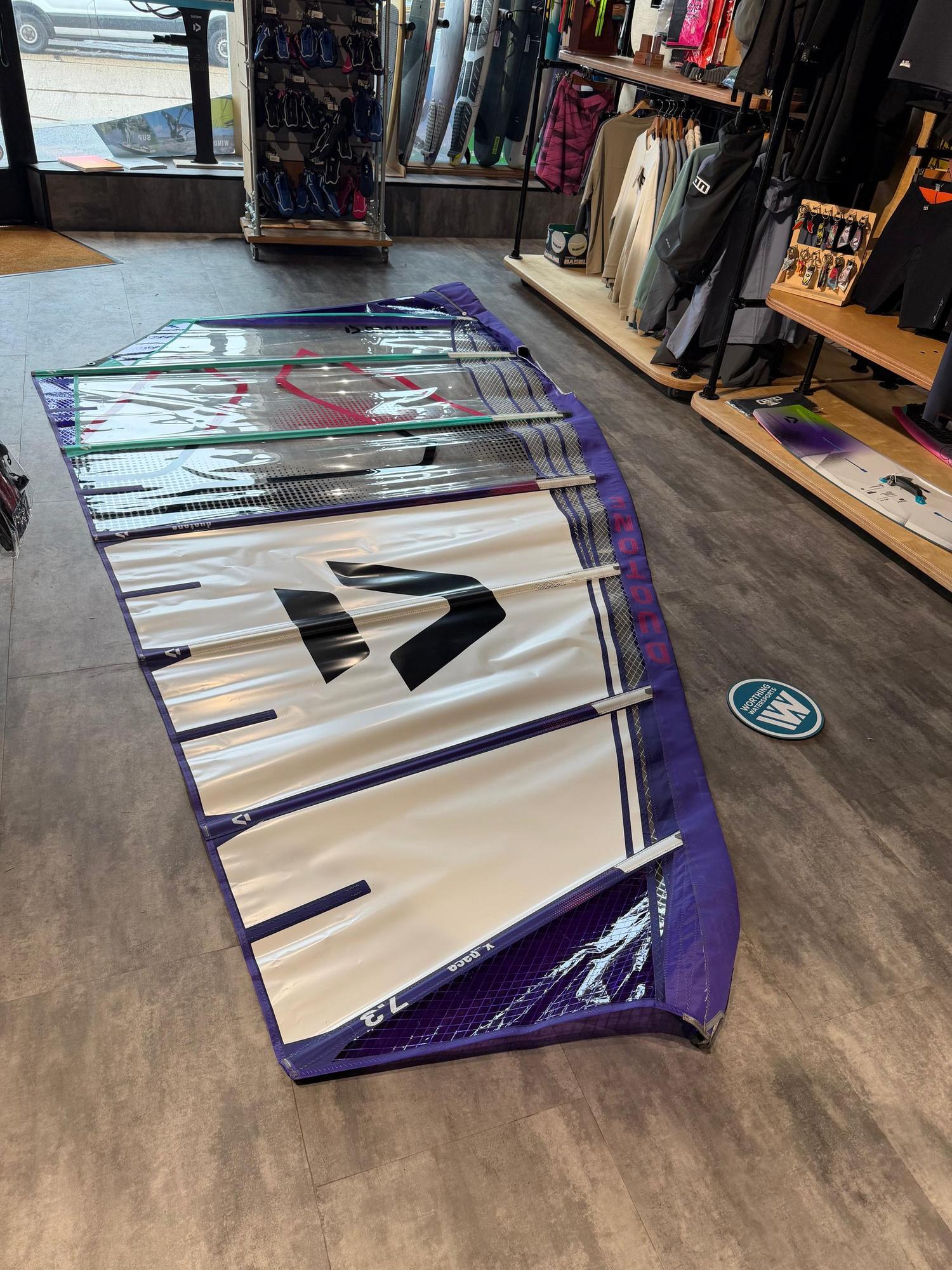 Used Duotone X_Pace 7.3m freerace windsurf sail in white and purple, laid flat on a shop floor.