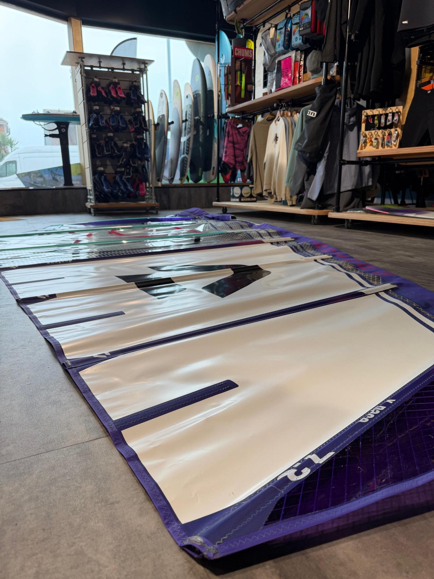 Used Duotone X_Pace 7.3m freerace windsurf sail in white and purple, laid flat on a shop floor.