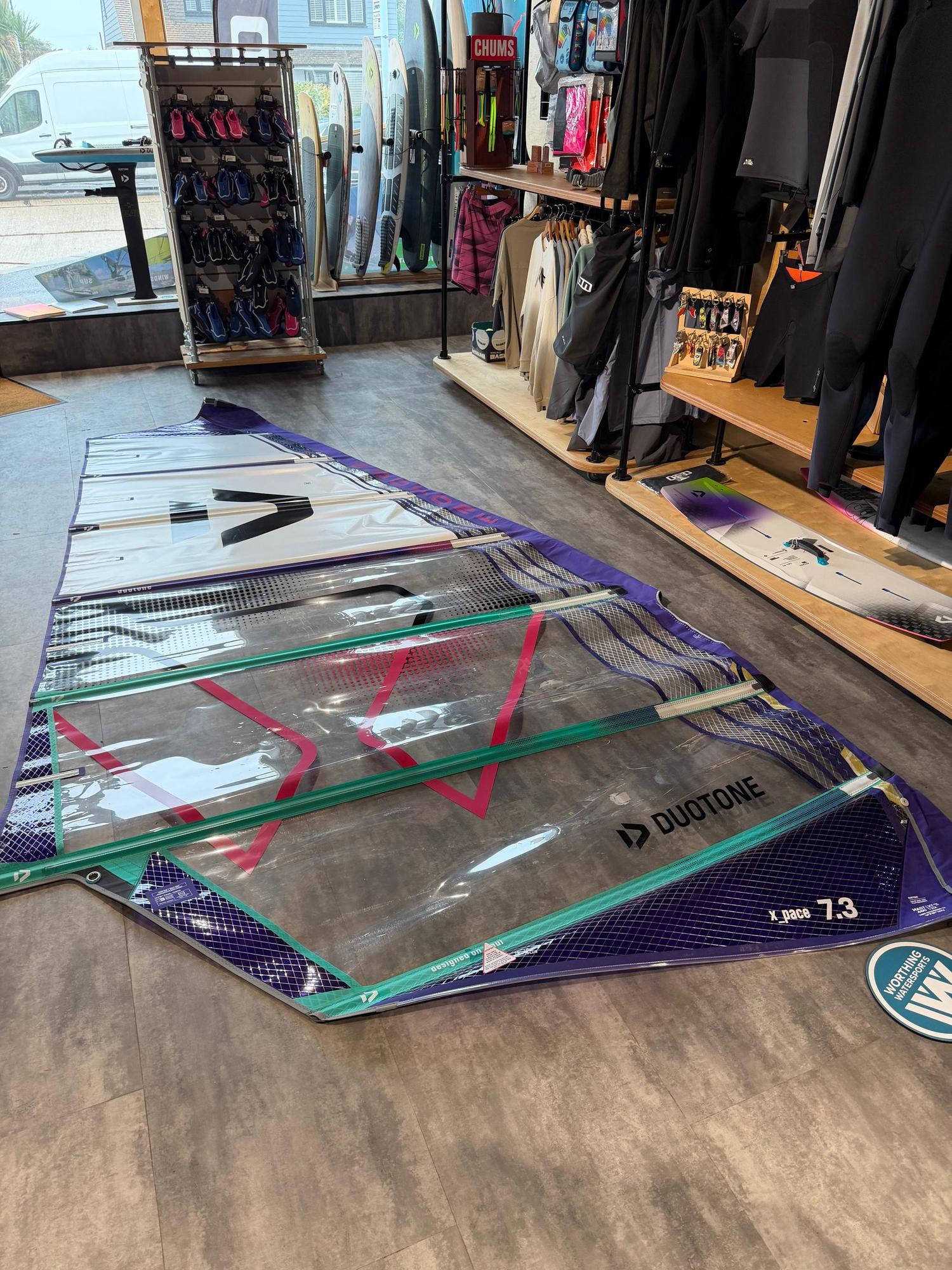 Used Duotone X_Pace 7.3m freerace windsurf sail in purple and white, laid flat on a shop floor.
