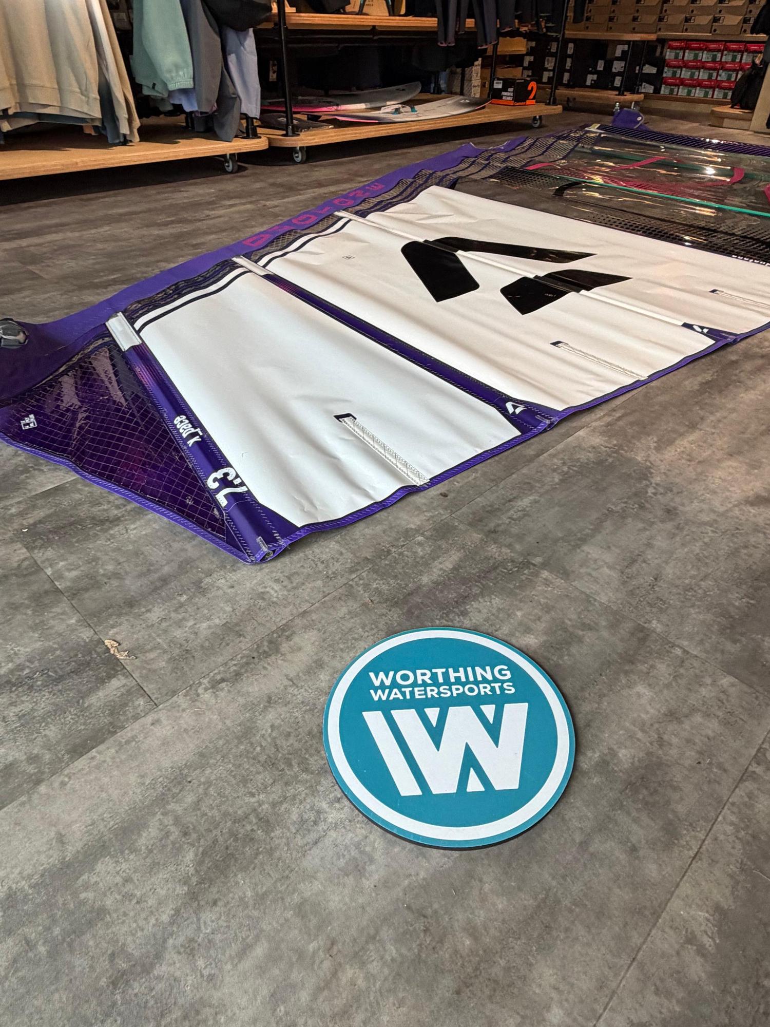 Used Duotone X_Pace 7.3m freerace windsurf sail in white and purple, laid out on a shop floor.