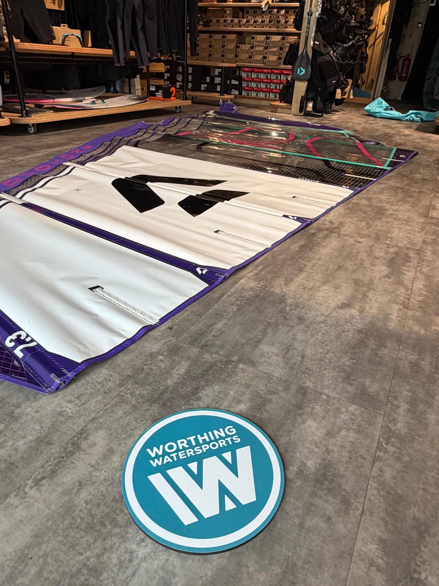 Used Duotone X_Pace 7.3m freerace windsurf sail in white and purple, laid flat on a shop floor.