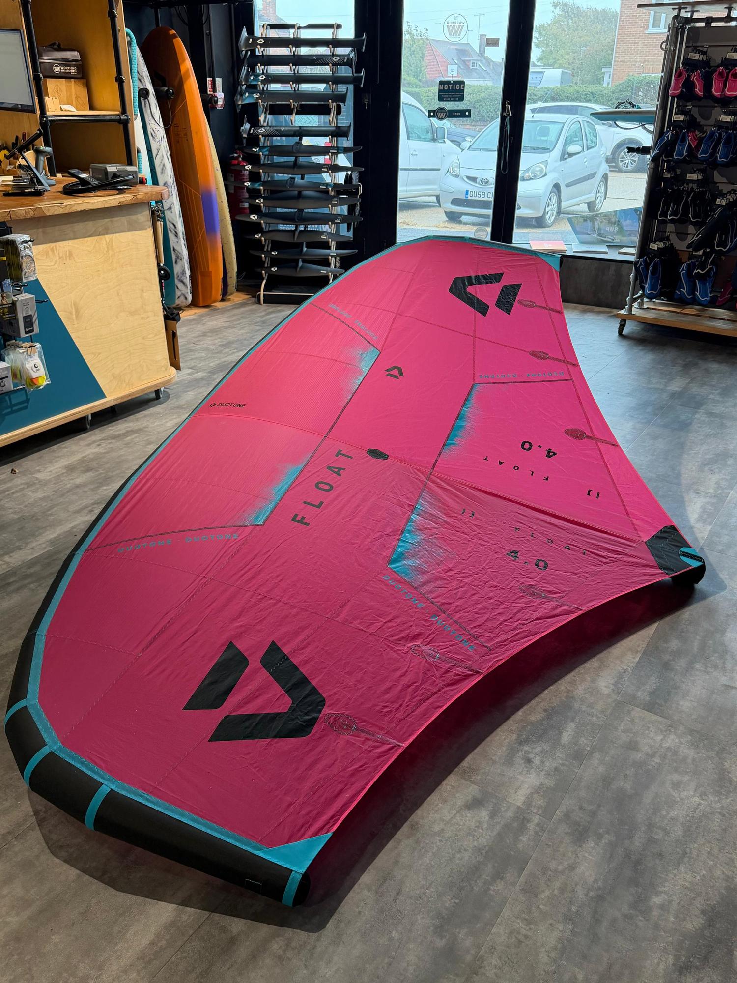Used Duotone Float 4m wave wing in pink with black branding, laid flat on a shop floor with boom and leash included.