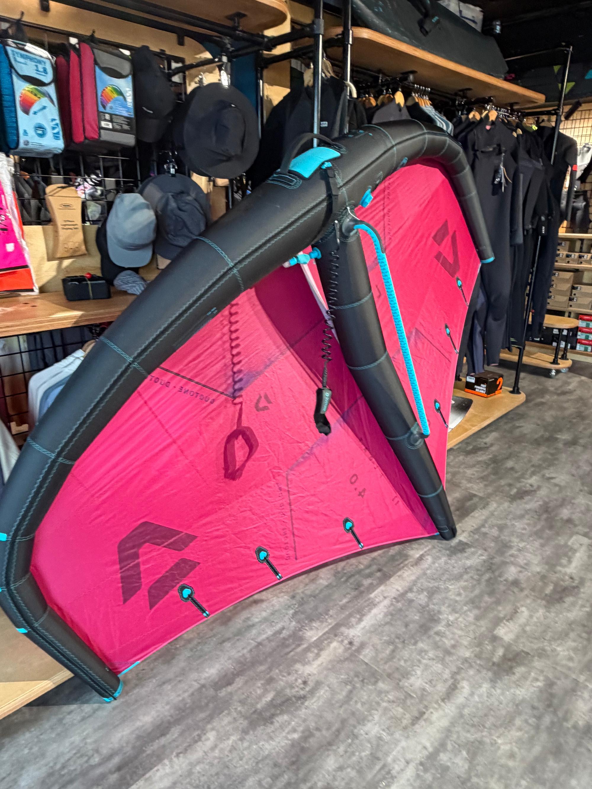 Used Duotone Float 4m wave wing in pink and black with boom and leash, displayed in a retail shop.