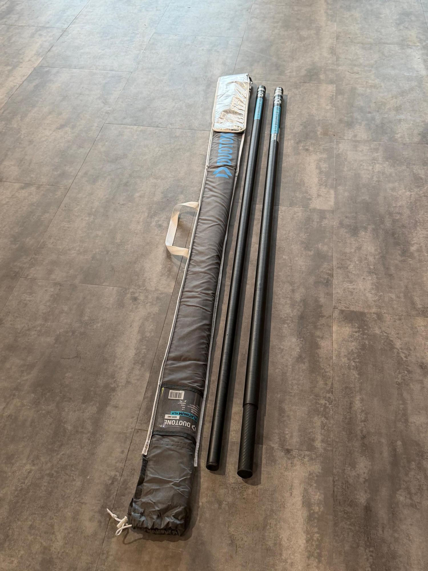Used Duotone Platinum SLS 340cm RDM windsurfing mast in two pieces with its original branded carry bag on a grey floor.