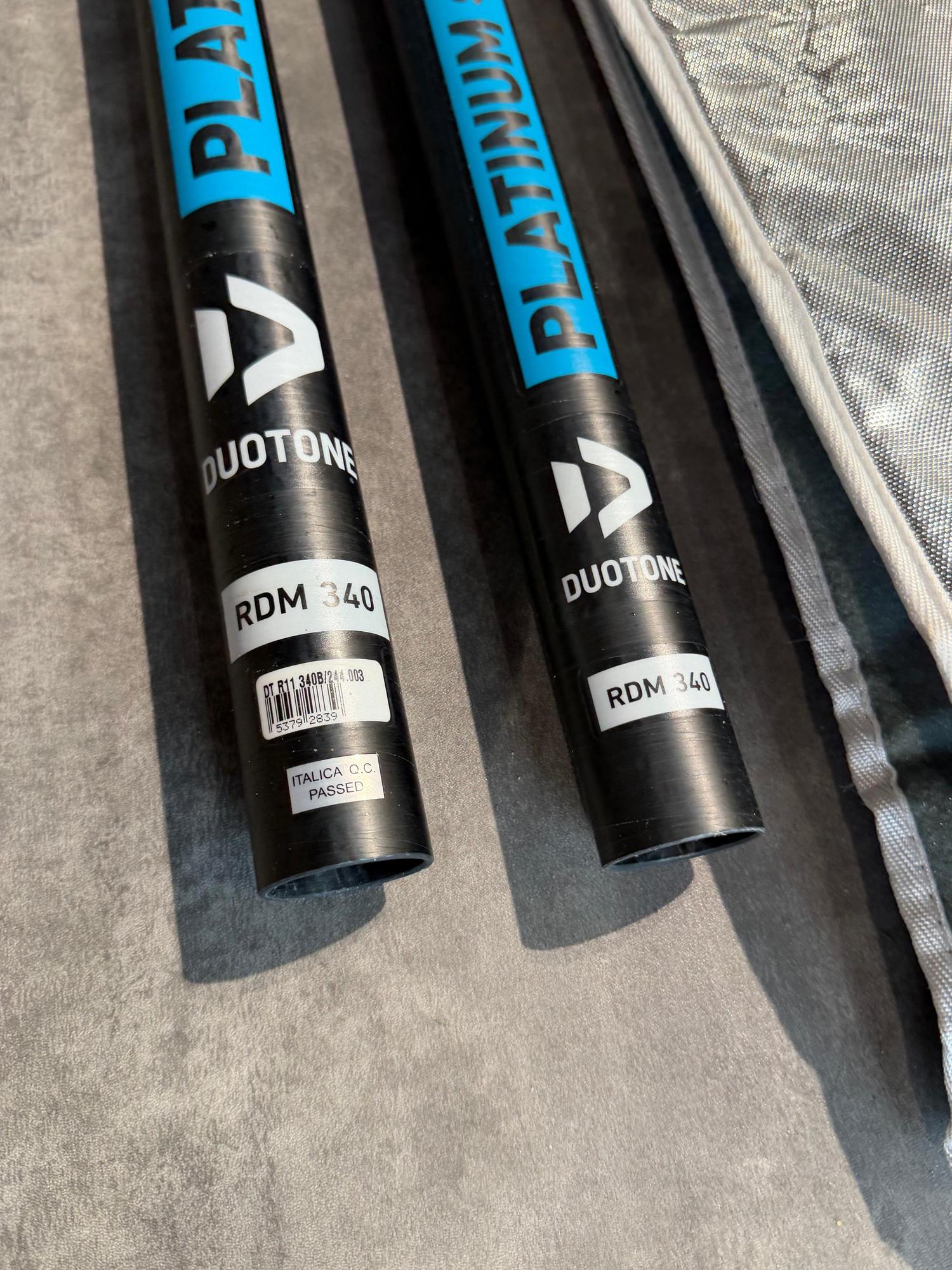Two-piece black carbon Duotone Platinum SLS RDM 340 windsurfing mast sections with blue branding and quality control labels.
