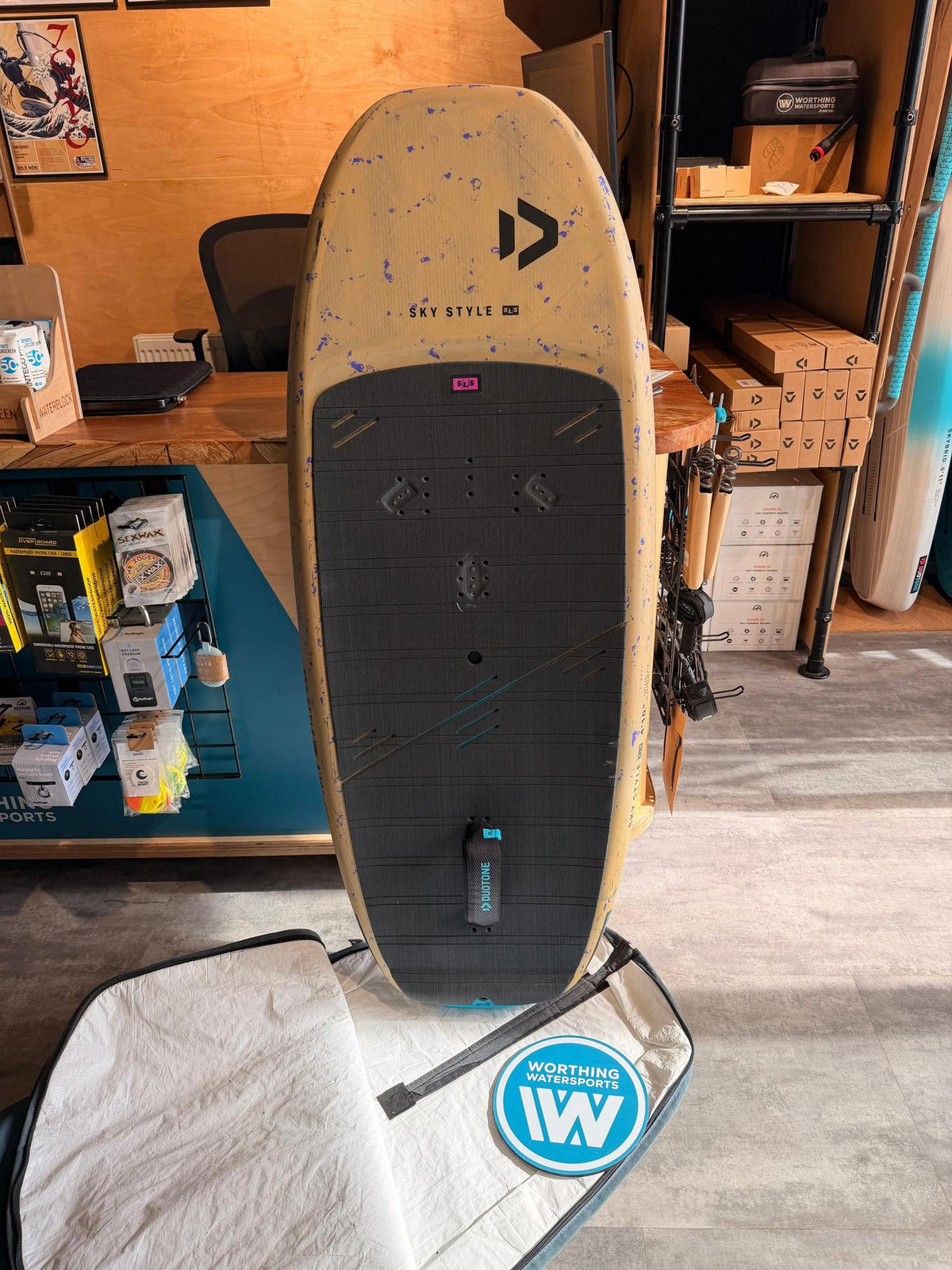 Used Duotone Sky Style SLS 2026 65L wing foil board in beige with blue speckles and a black deck pad, standing upright.
